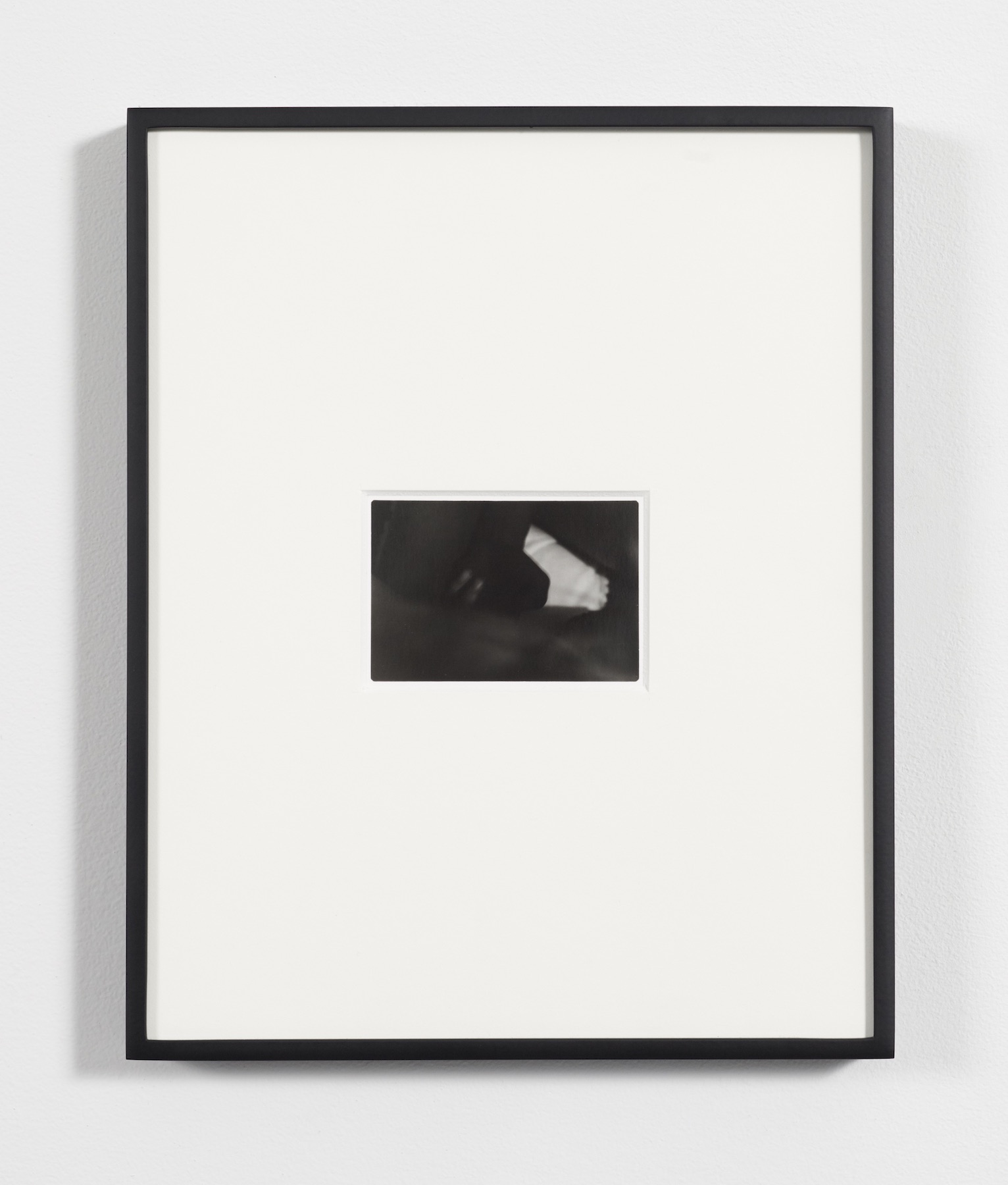 A dark image of indecipherable body parts. Surrounded by a large matte and frame.
