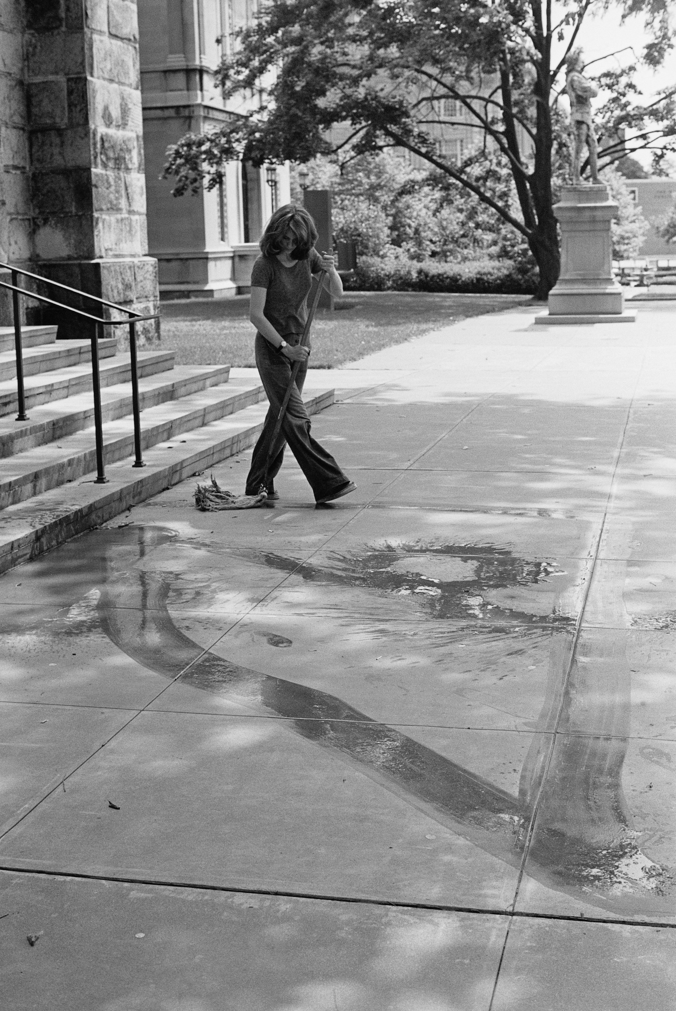 Woman mopping sidewalk outside of building in black and white.