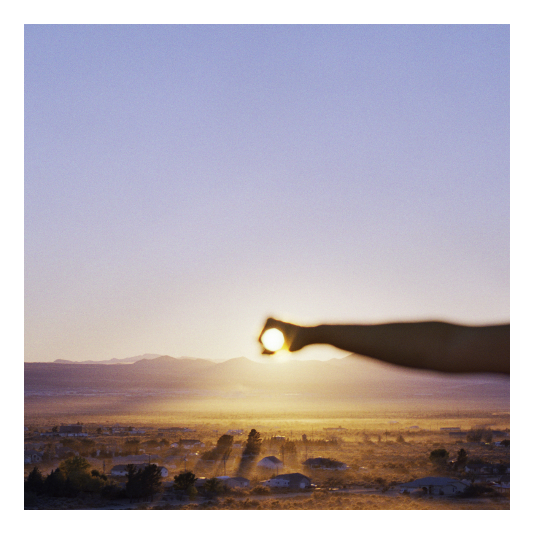 a hand reaching out and covering the sun on a low horizon