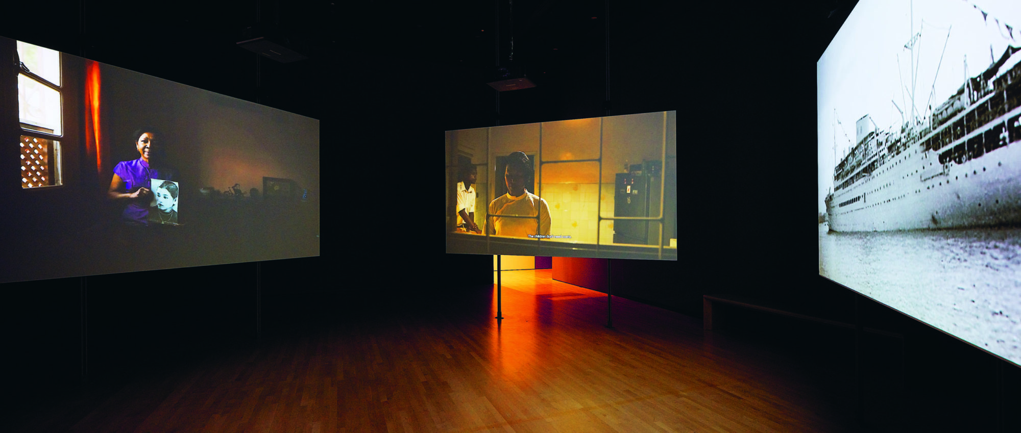 Installation view of Tuan Nguyen's work in which three videos play simultaneously in the same room
