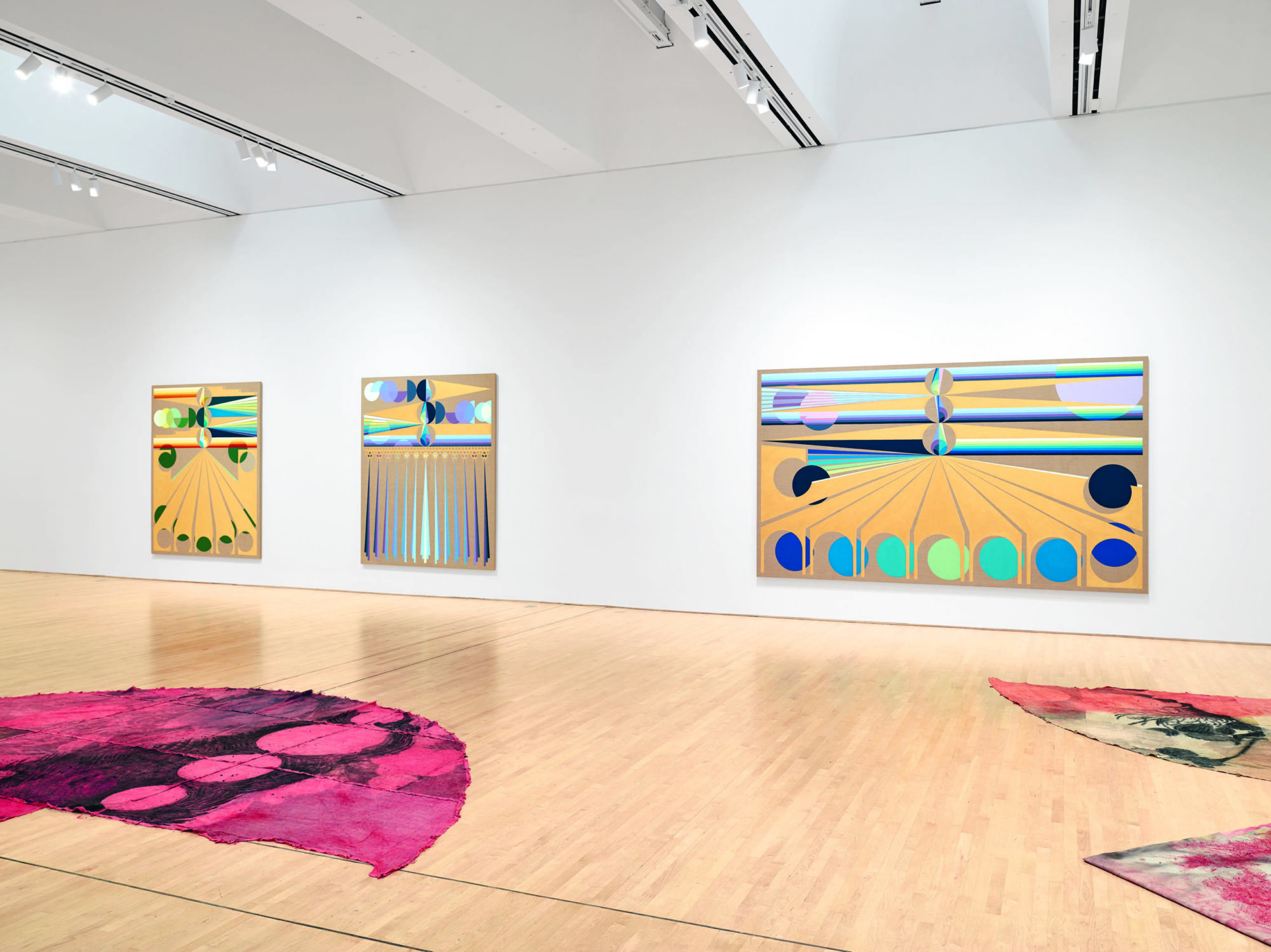 Installation shot of Soft Power at SFMOMA; pieces containing both organic and geometric figures hand on the walls and lay on the wooden floor