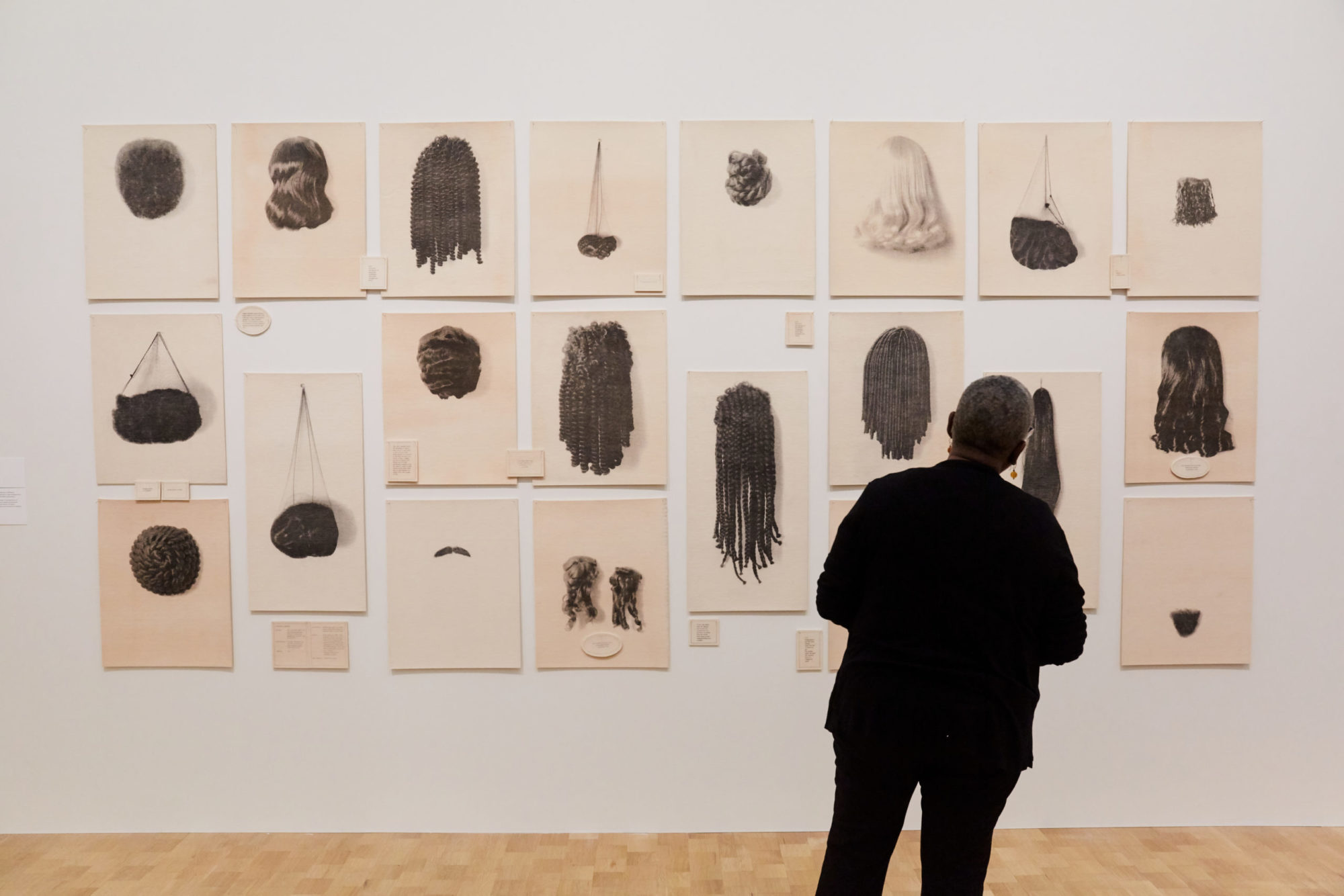 a patron stands in front of a wall of images of varying sizes and shapes featuring depictions of black women hair-styles