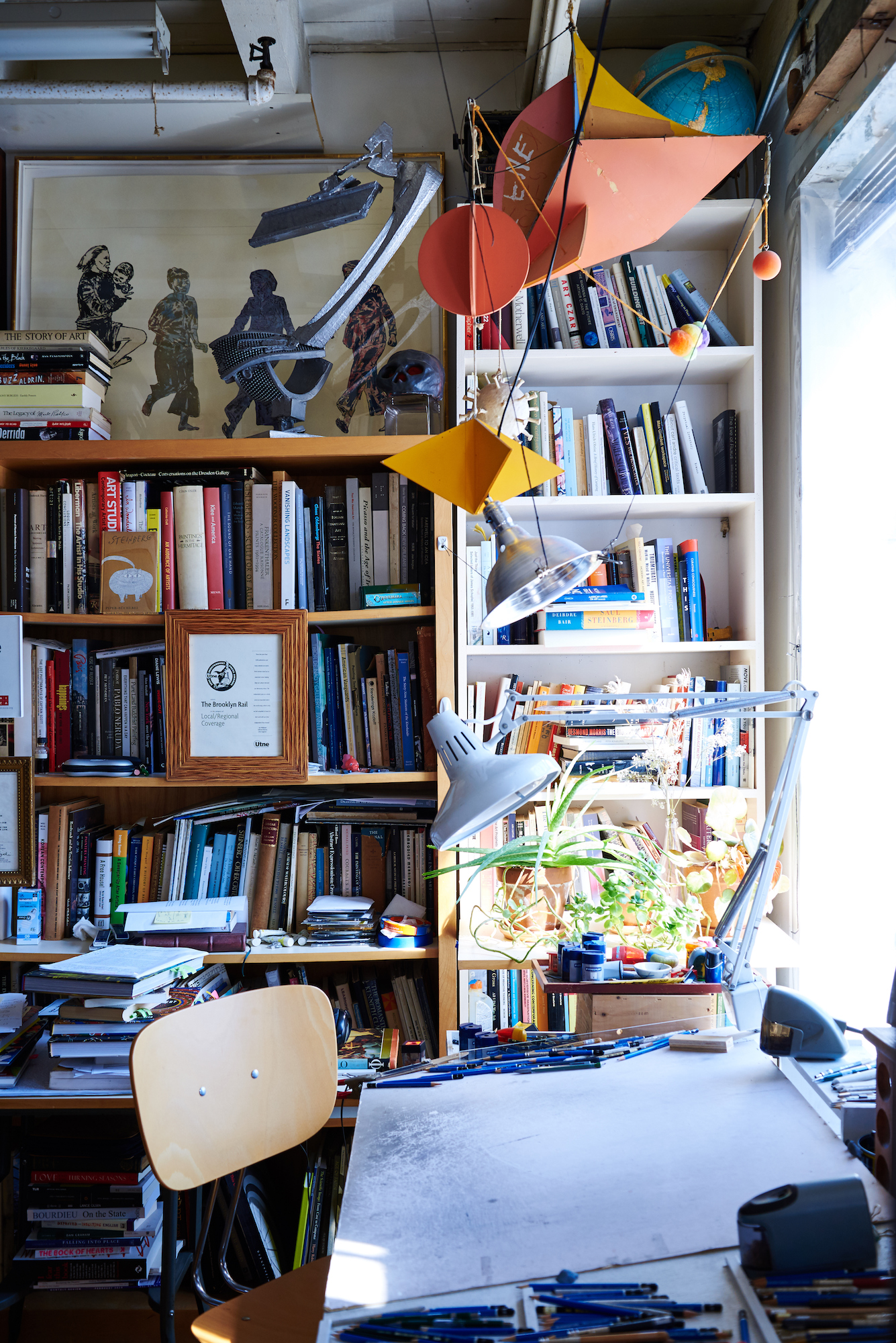 A drawing table with books in the background and a mobile hanging from the ceiling.