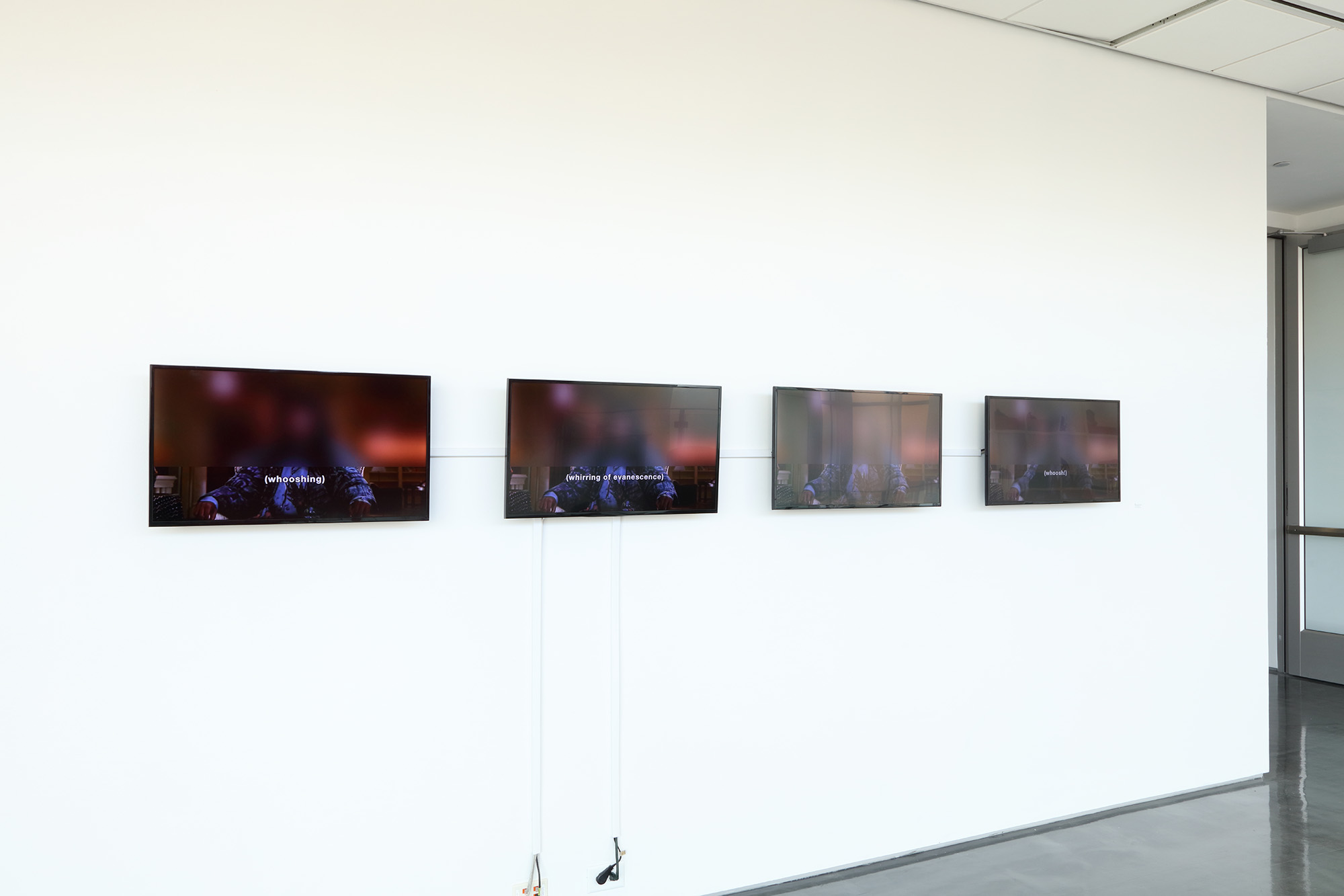 Four TV screens hanging up on a white wall