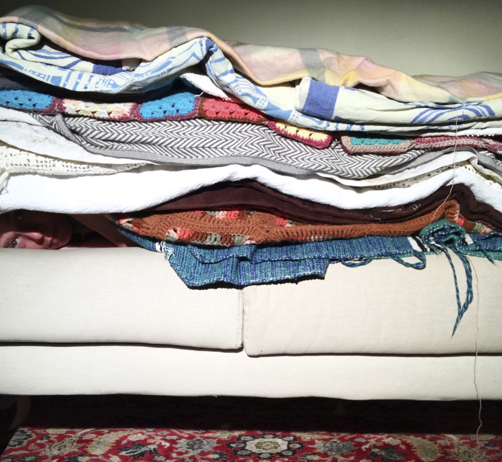 a person lying on a couch with numerous blankets stacked on top of them