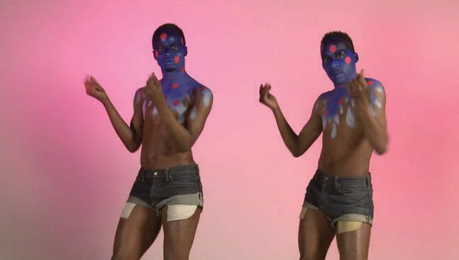 a screenshot from the music video Goodie Goodie, showing two people in shorts and body paint in motion