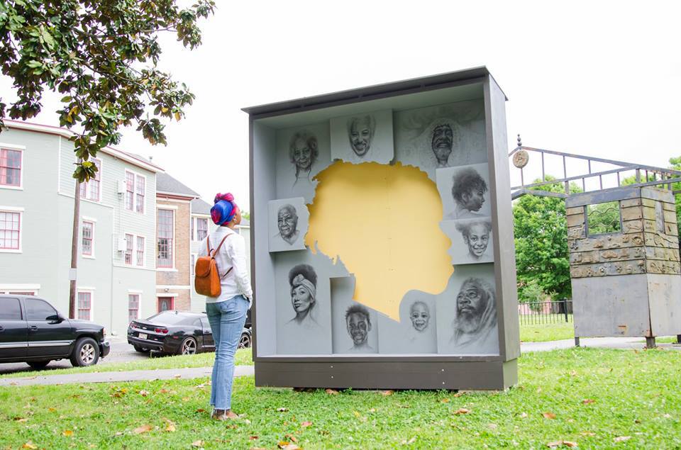 A photo of a woman observing a structure encasing the silhouette of a head surrounded by portraits.