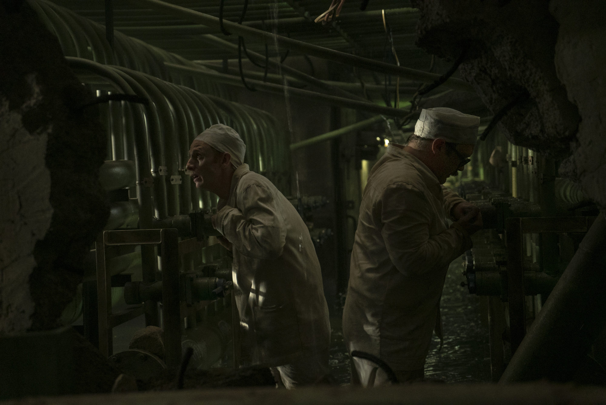 two people stand in a dark flooded hallway, attempting to shut off valves