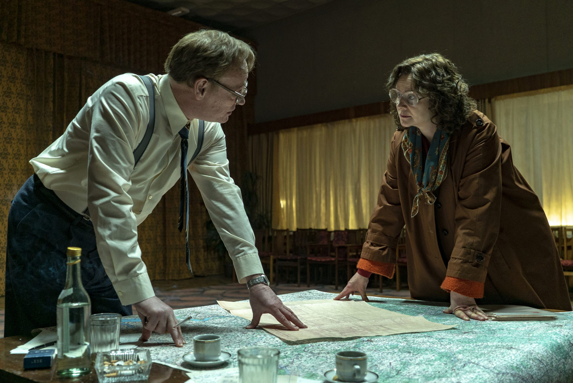 Jared Harris and Emily Watson stand over a desk which is covered with a map