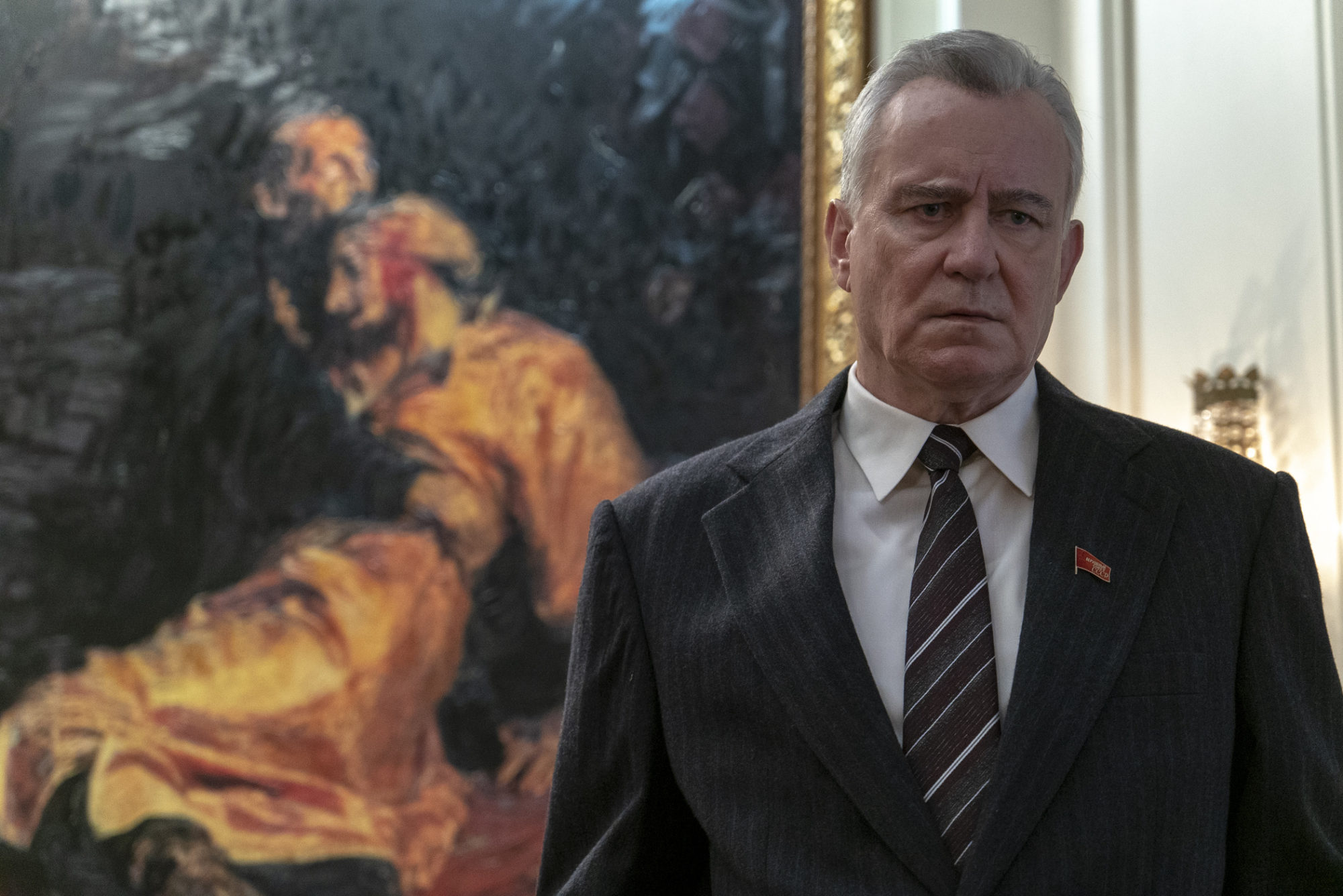 Stellan Skarsgard, in a suit, stands in front of the painting Ivan the Terrible with His Son Ivan