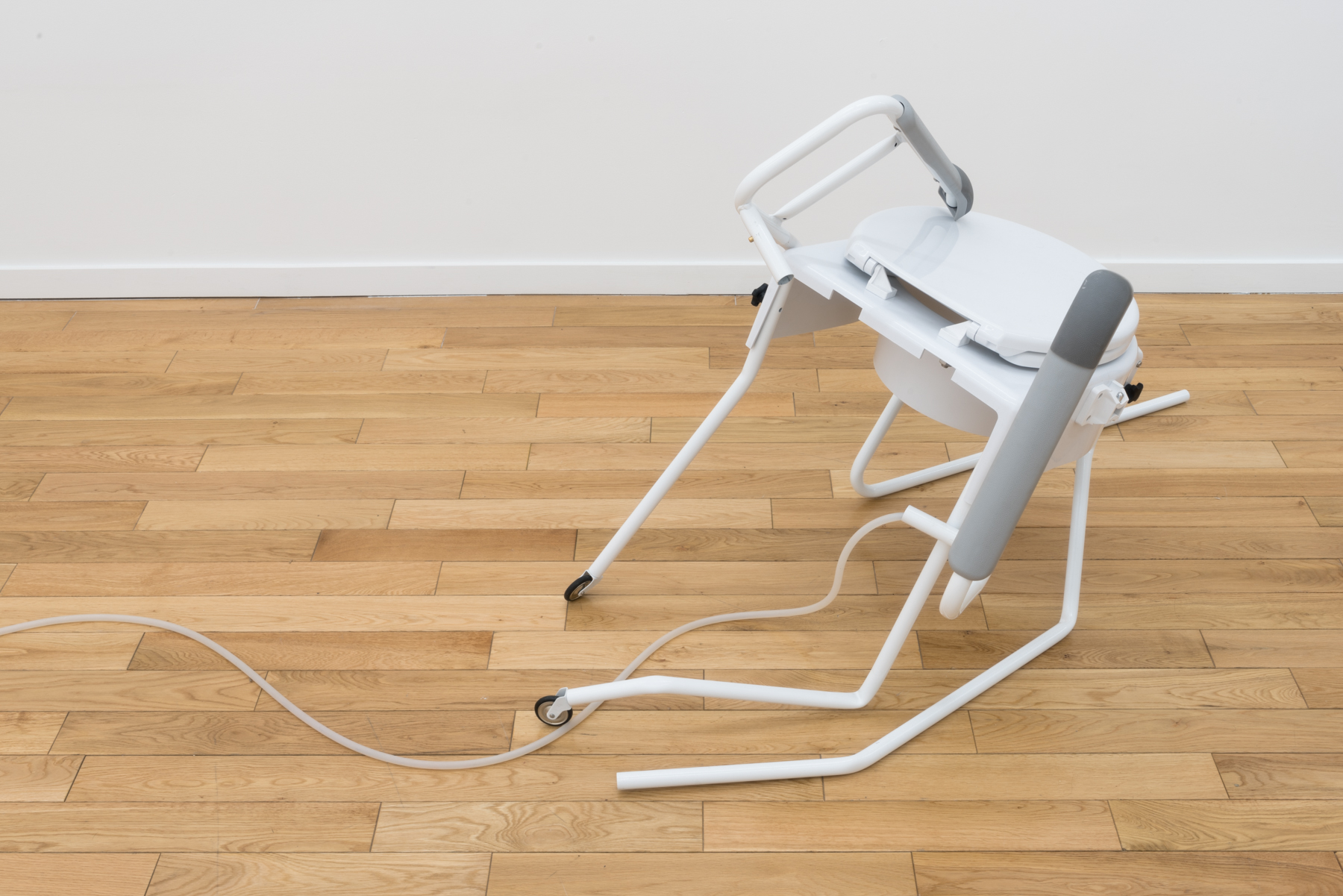 sculpture of a white twisted, collapsing chair with wheels on the bottom and a tube coming off to the left