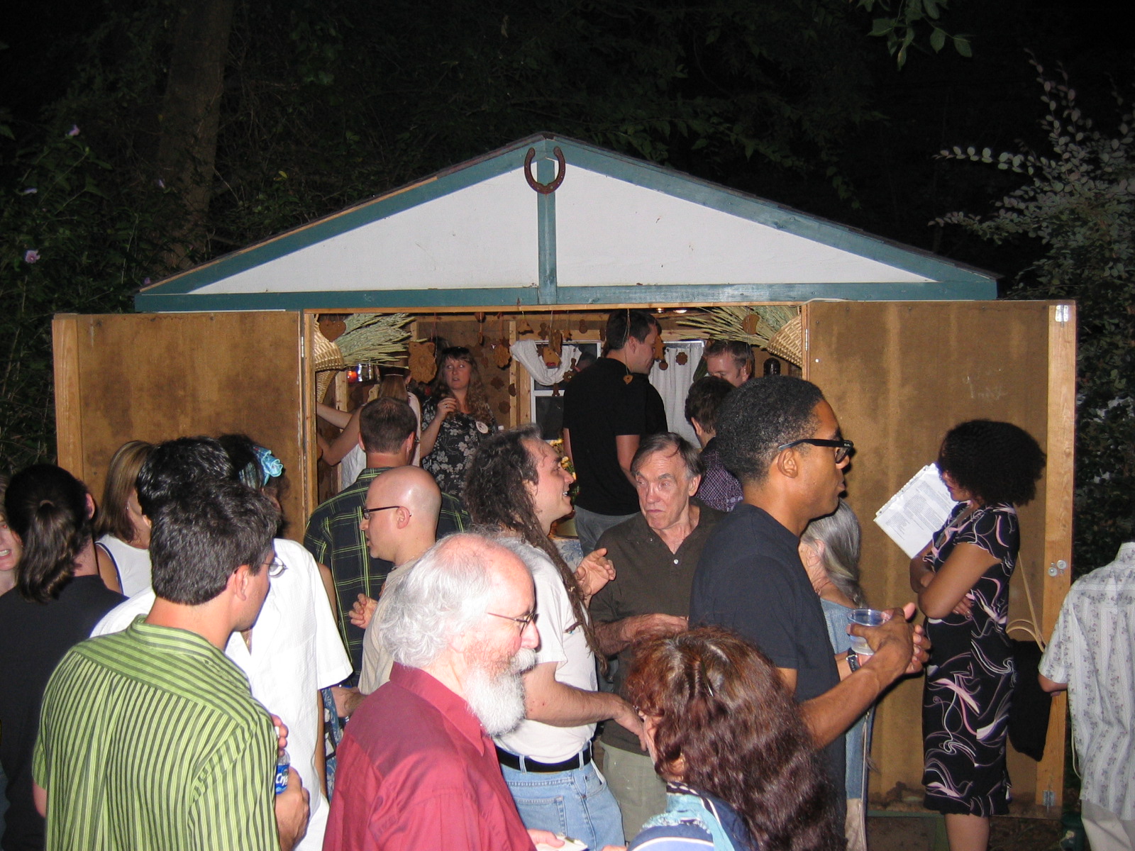 An image of a group of individuals standing inside and outside a shed. It's dark outside.