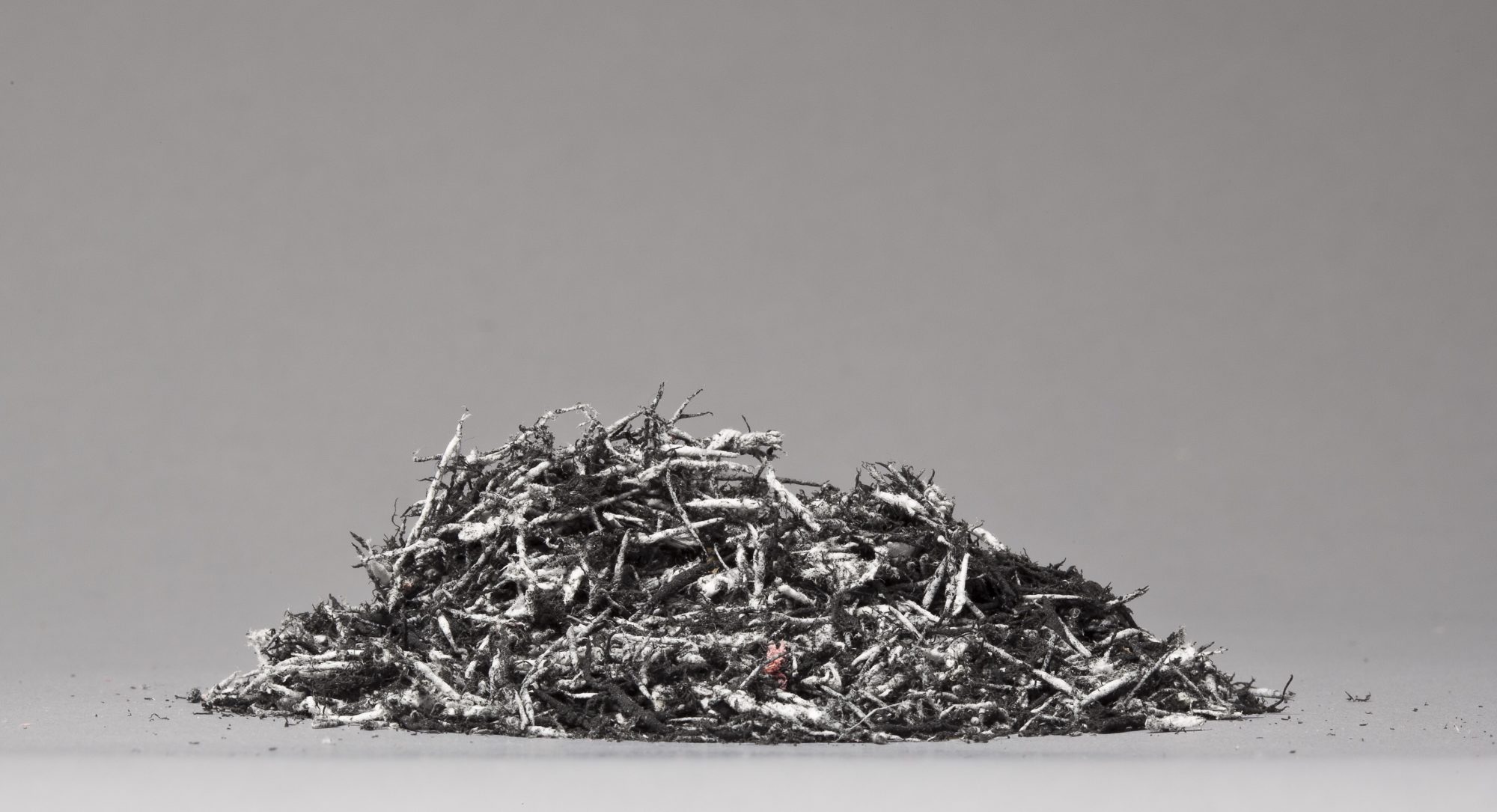 A pile of used eraser shavings on a matte gray surface, just off center from the middle of the stack there is a single pink eraser