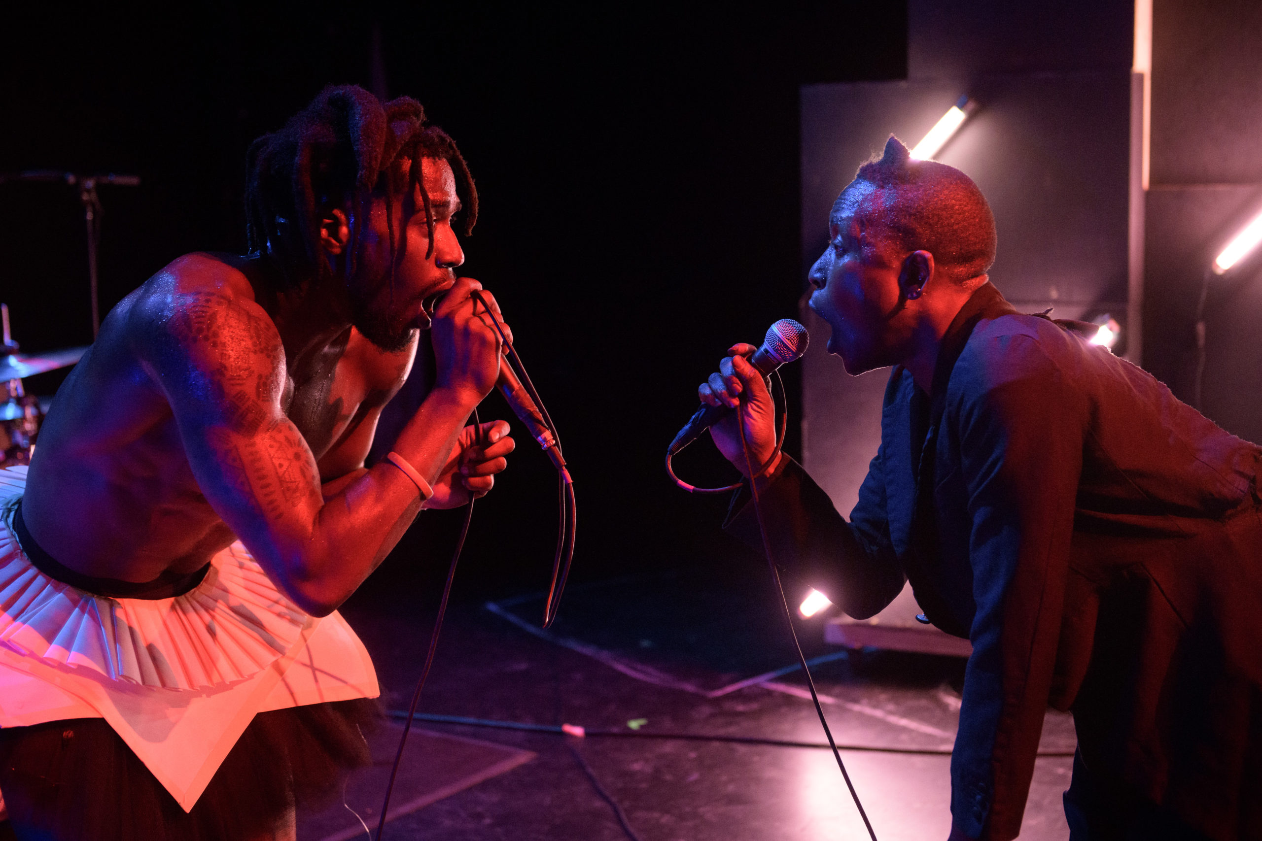 two performers with microphones and blue and red lighting