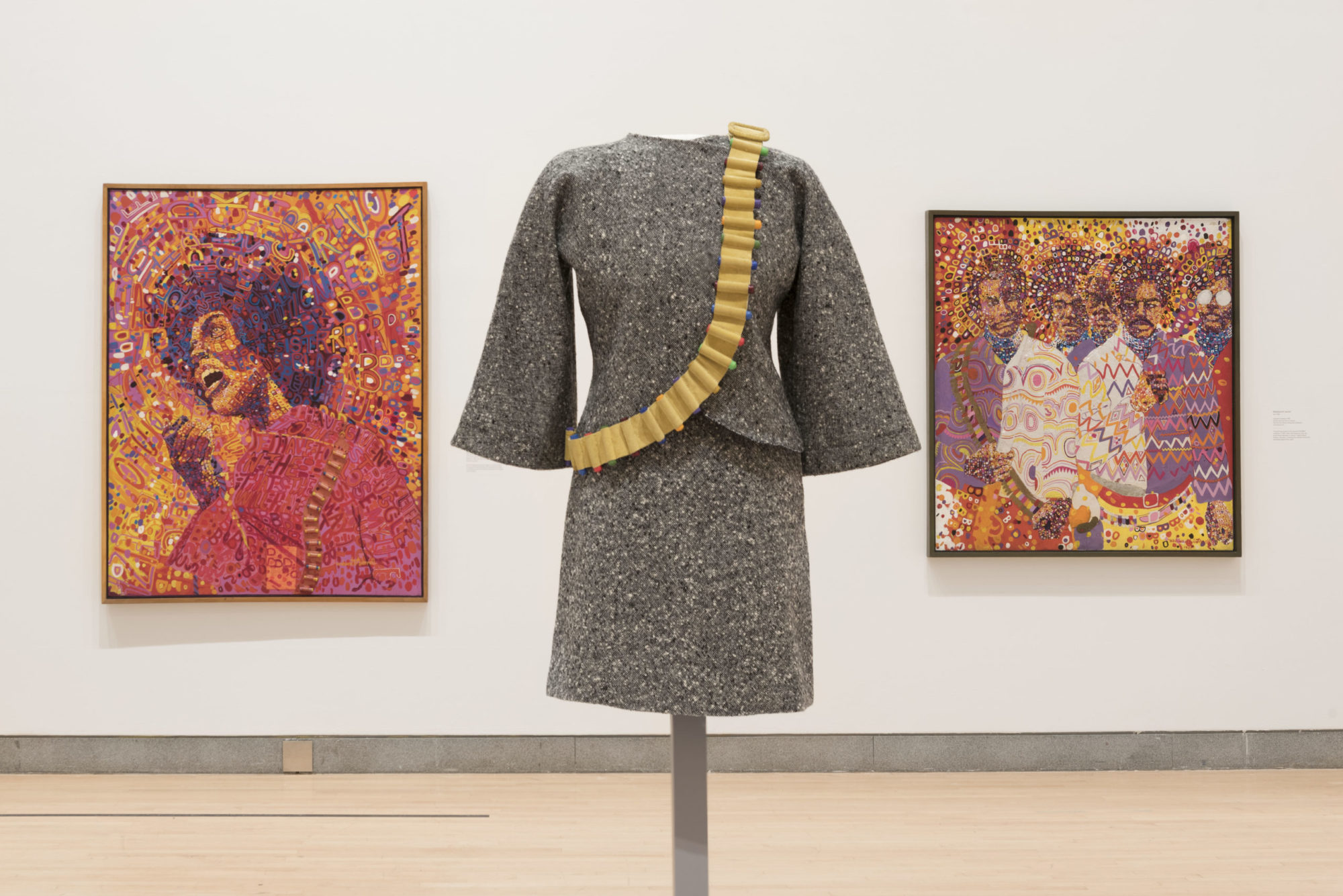 Installation shot of the show 'Soul of a Nation;' a dress with multi-colored bullet belt is center foreground between two colorful paintings depicting African American people
