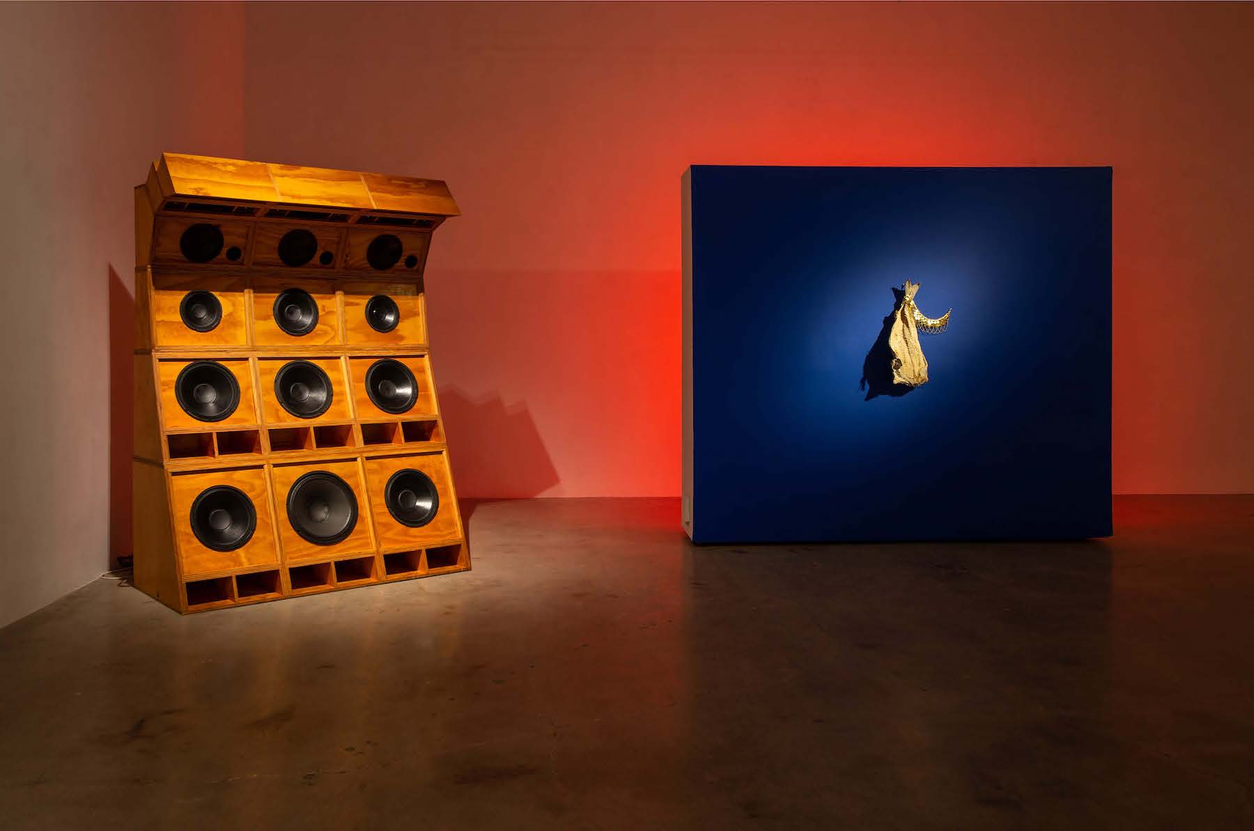 A large speaker placed next to a blue square that has an object attached to the middle.