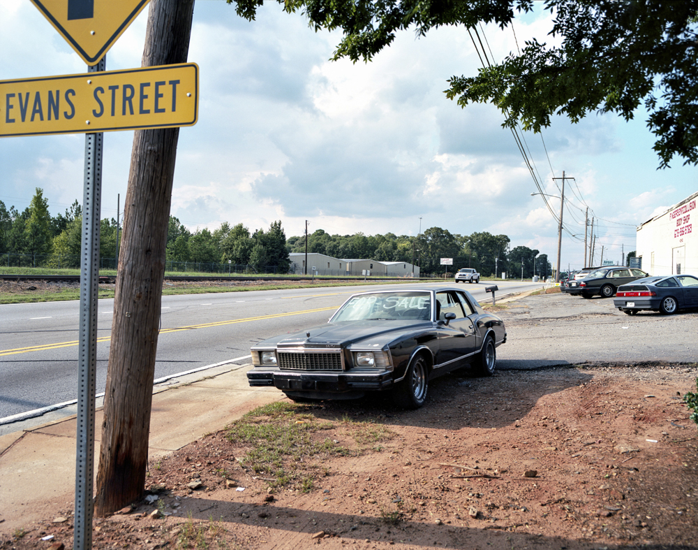 A car for sale by a road and a traffic sign