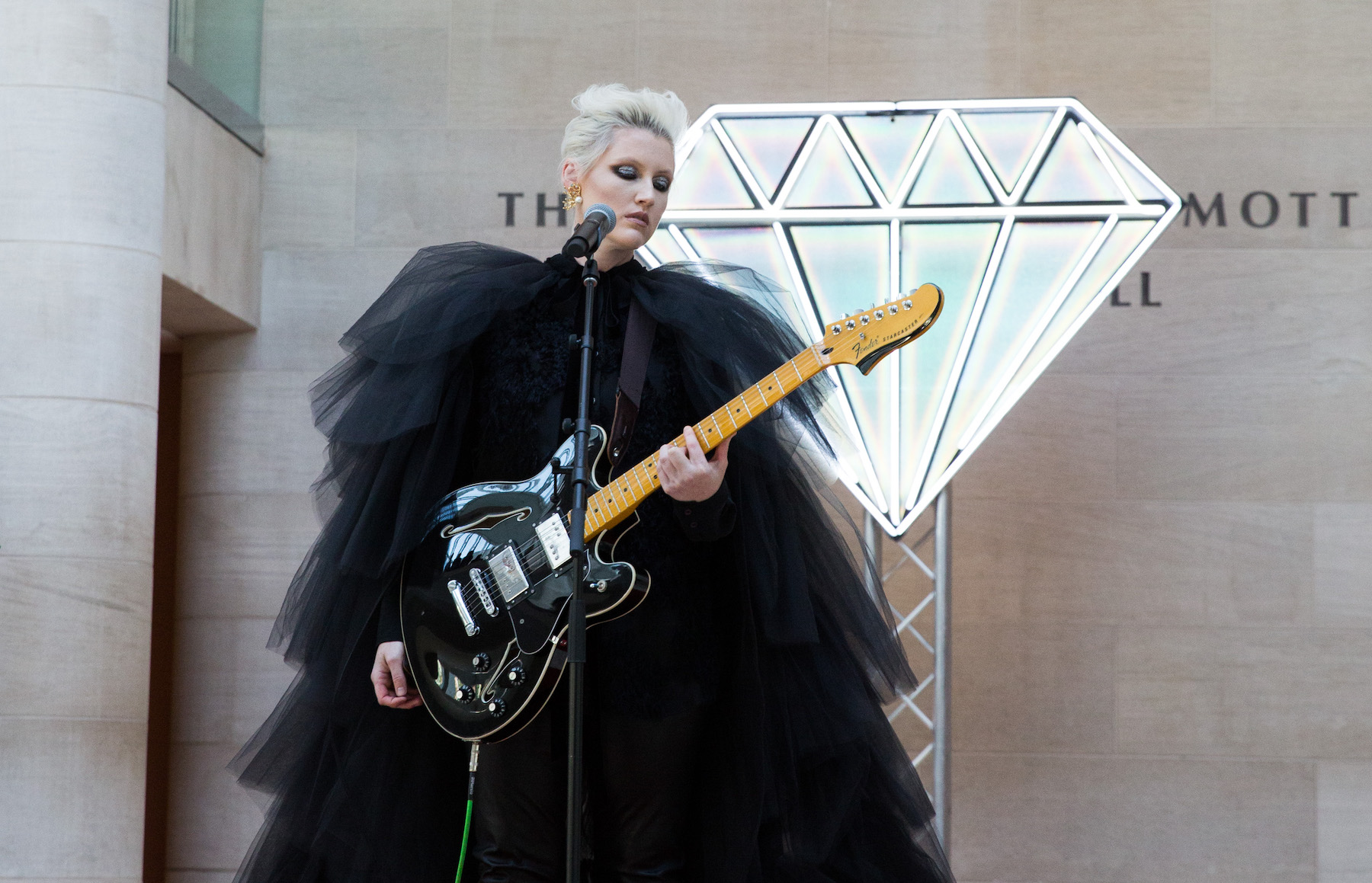 Women in black, frilly dress playing guitar at a microphone.