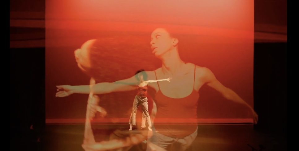 Double-exposed image of person (Gesel Mason) on stage standing against a red backdrop with both arms outstretched at her sides, and two faded images of her on top of that mid-movement/dancing.
