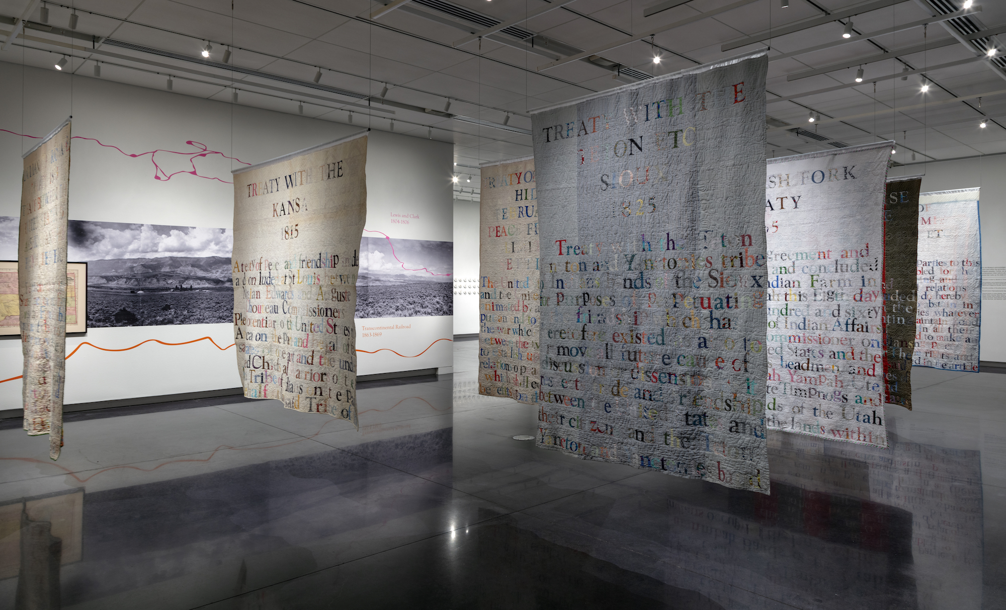 Quilts with writing hanging in a row from the ceiling.