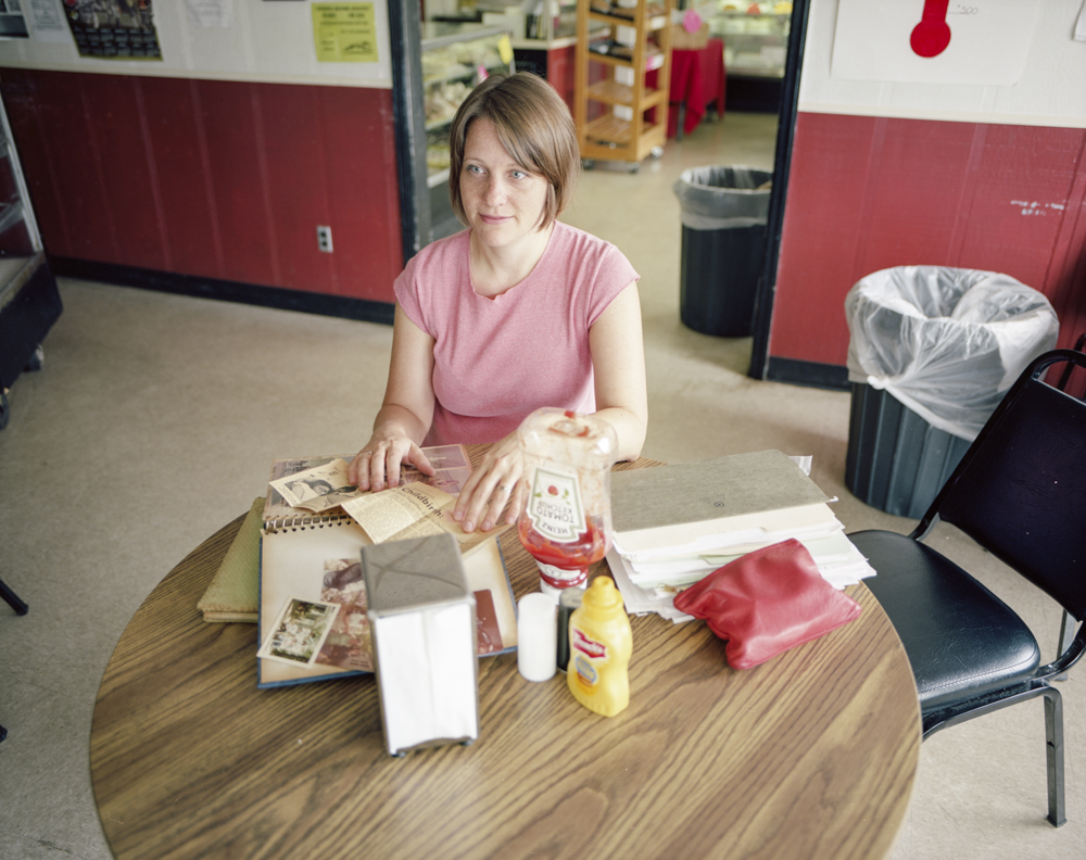 A woman sits at a table with a newspaper clipping and scrapbook