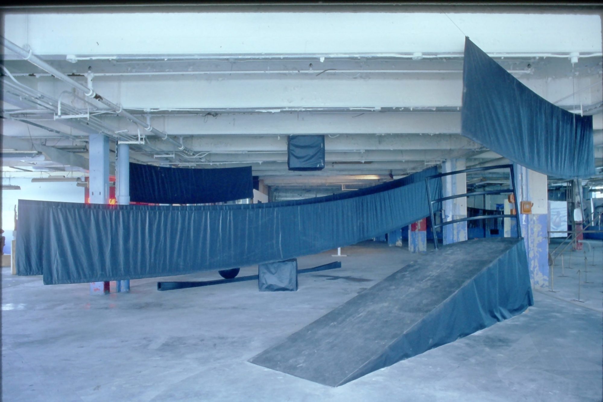 A photograph of an art installation with suspended black pieces of cloth and a black ramp.