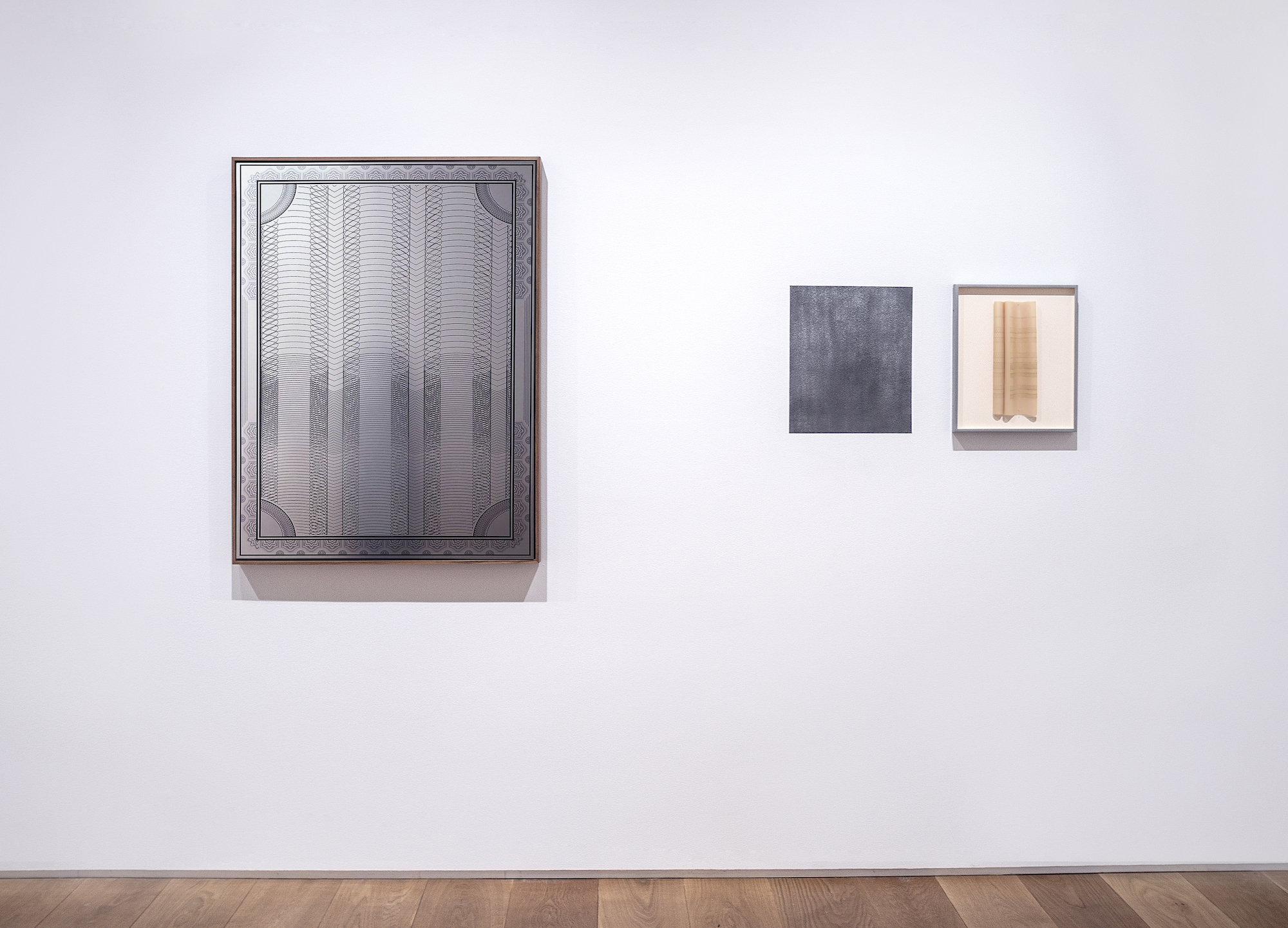 One mirrored drawing hangs on the wall to the left while two smaller drawings hang together to the right. One of the two is a slate colored paper and the other is a framed piece of parchment framed and pinned to the center.