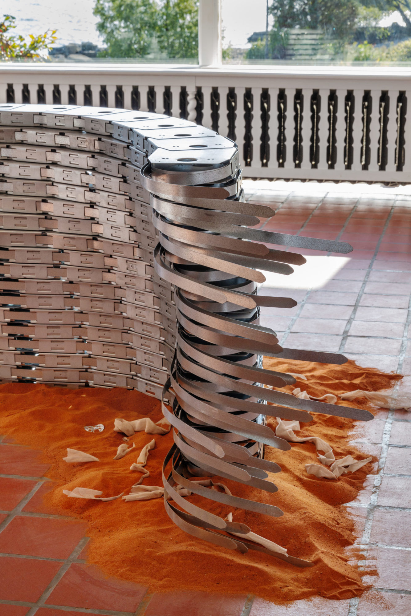shot of part of Laurie Kang's work, 'Worm.' Silver aluminum sculpture sit on top of an orange pile of sand