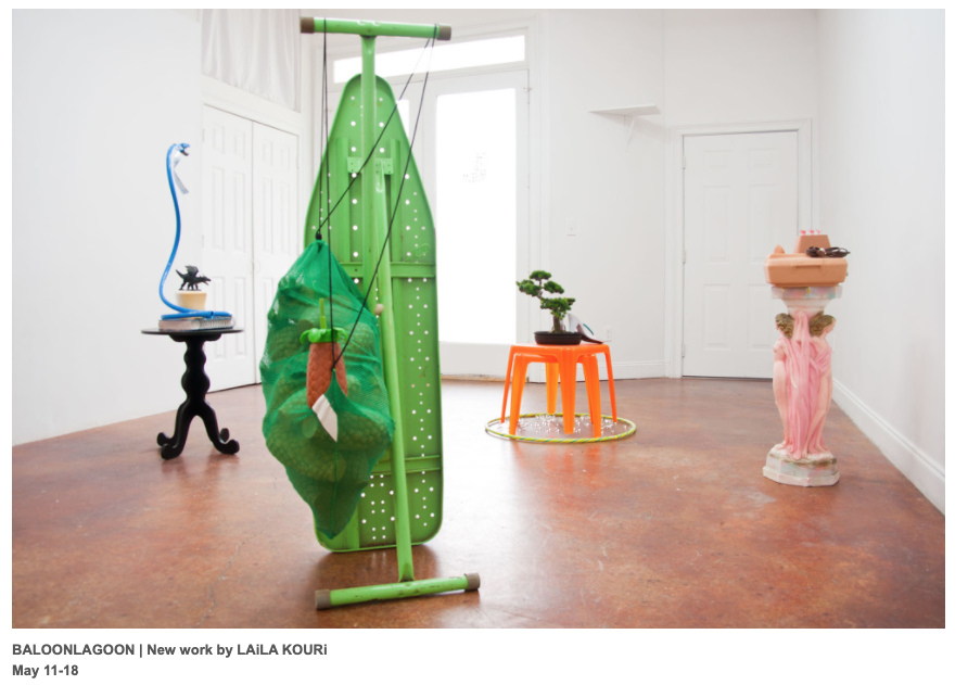 A photograph of an installation view with several sculptures, including objects that resemble a green clothing iron and a tree. The sculptures are green, orange, blue and pink.