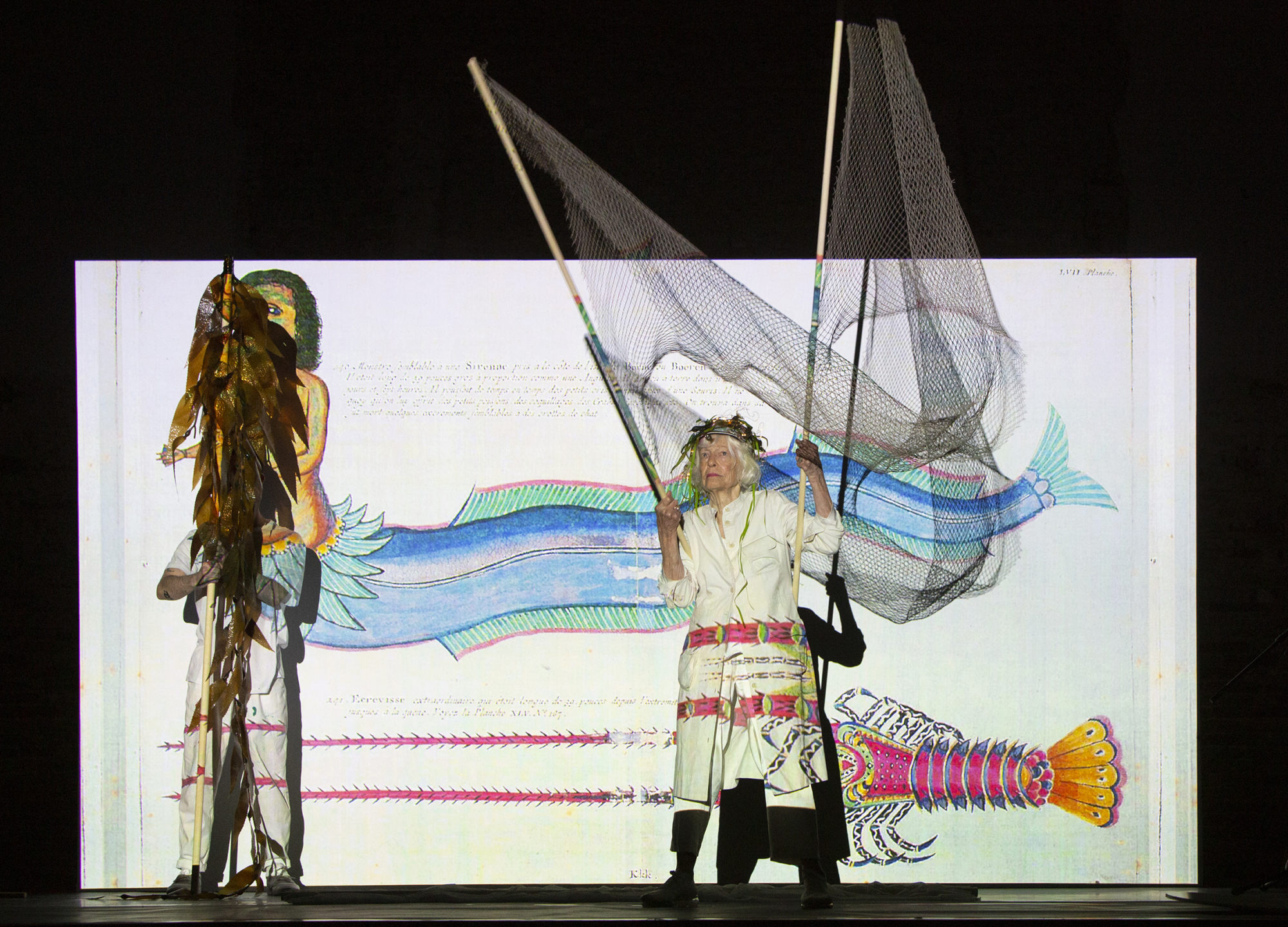Joan Jonas performing with nets and projections in front of a white screen.