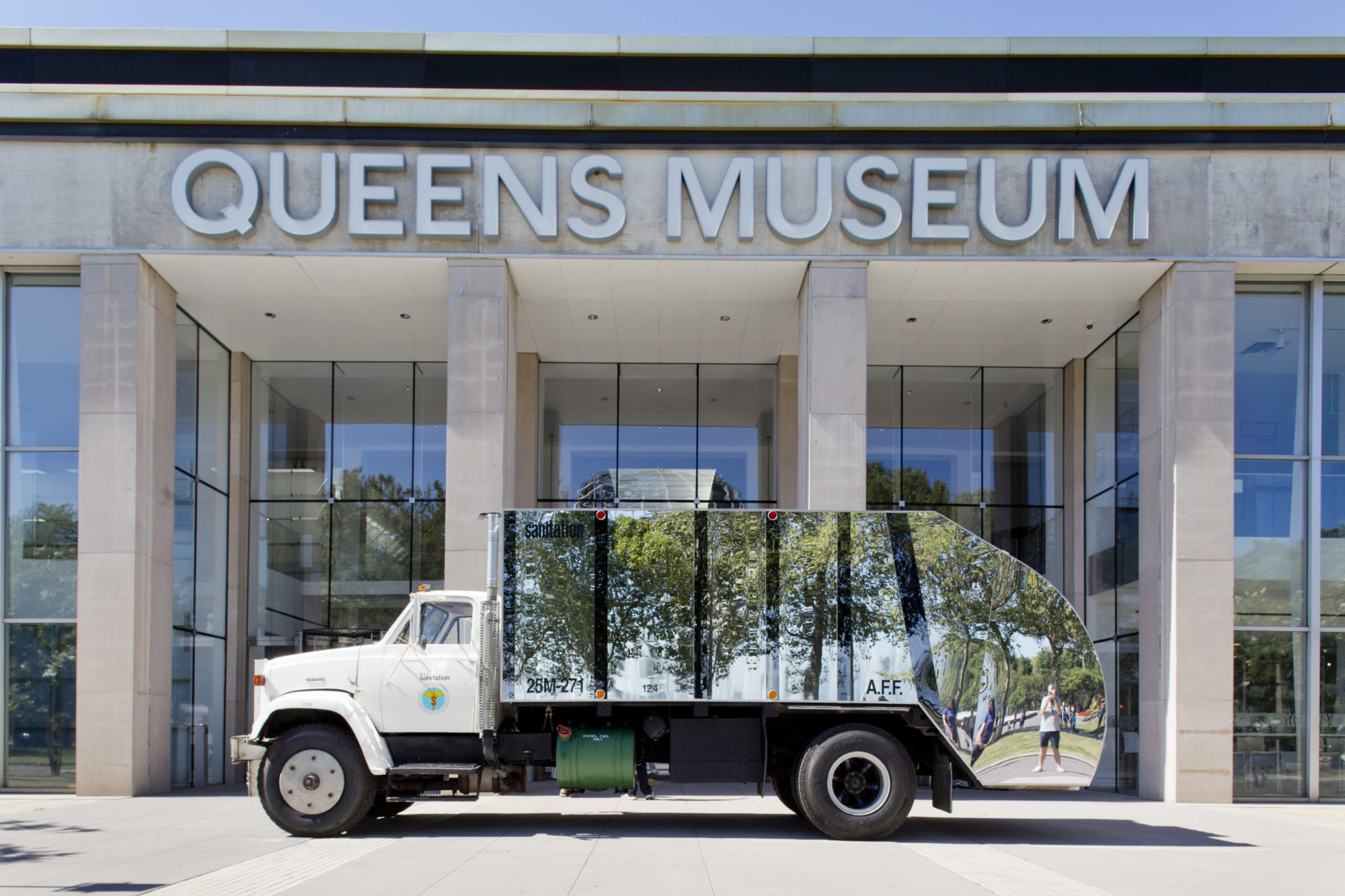 Garbage truck with reflective side in front of Queens Museum.