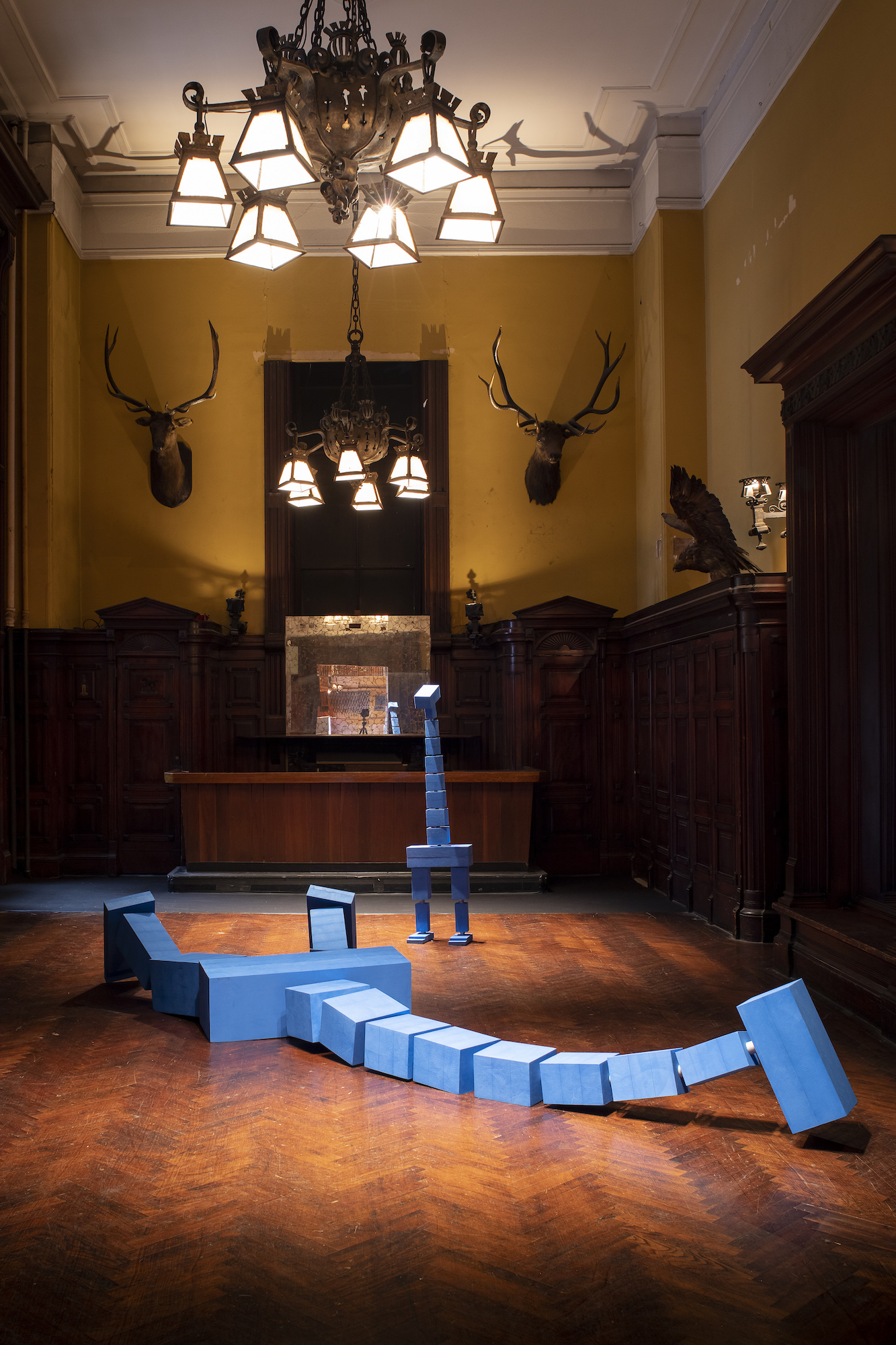 A blue, square shaped sculpture laying on the floor of a large room.