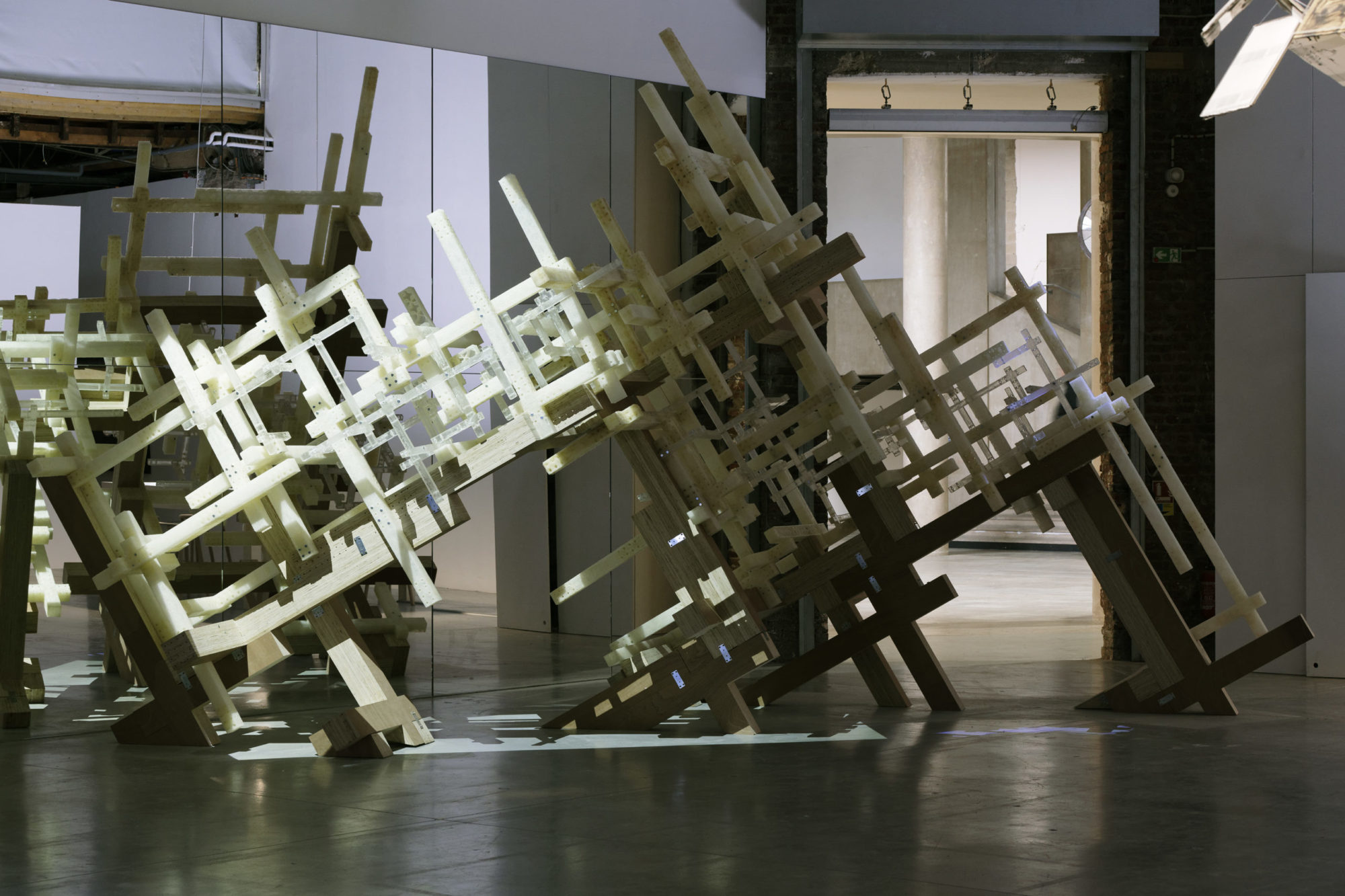 various materials make up a capsized jungle-gym grid sculpture which sits on the ground in a semi-sunlit room