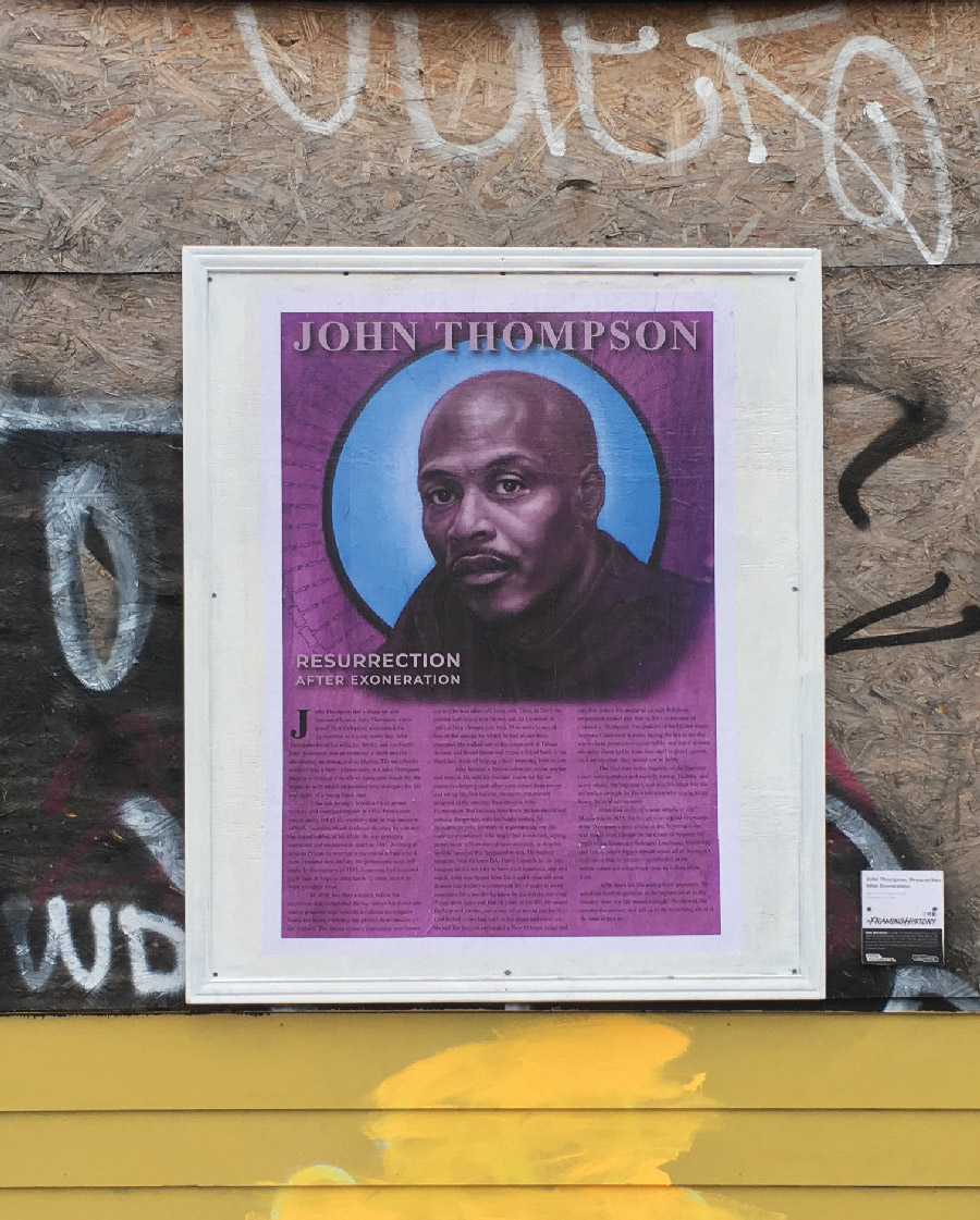 A photo of a framed poster hanging on a graffitied wall.