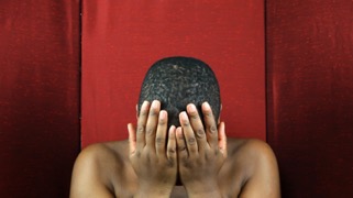 person in front of red backdrop holds their face in their hands