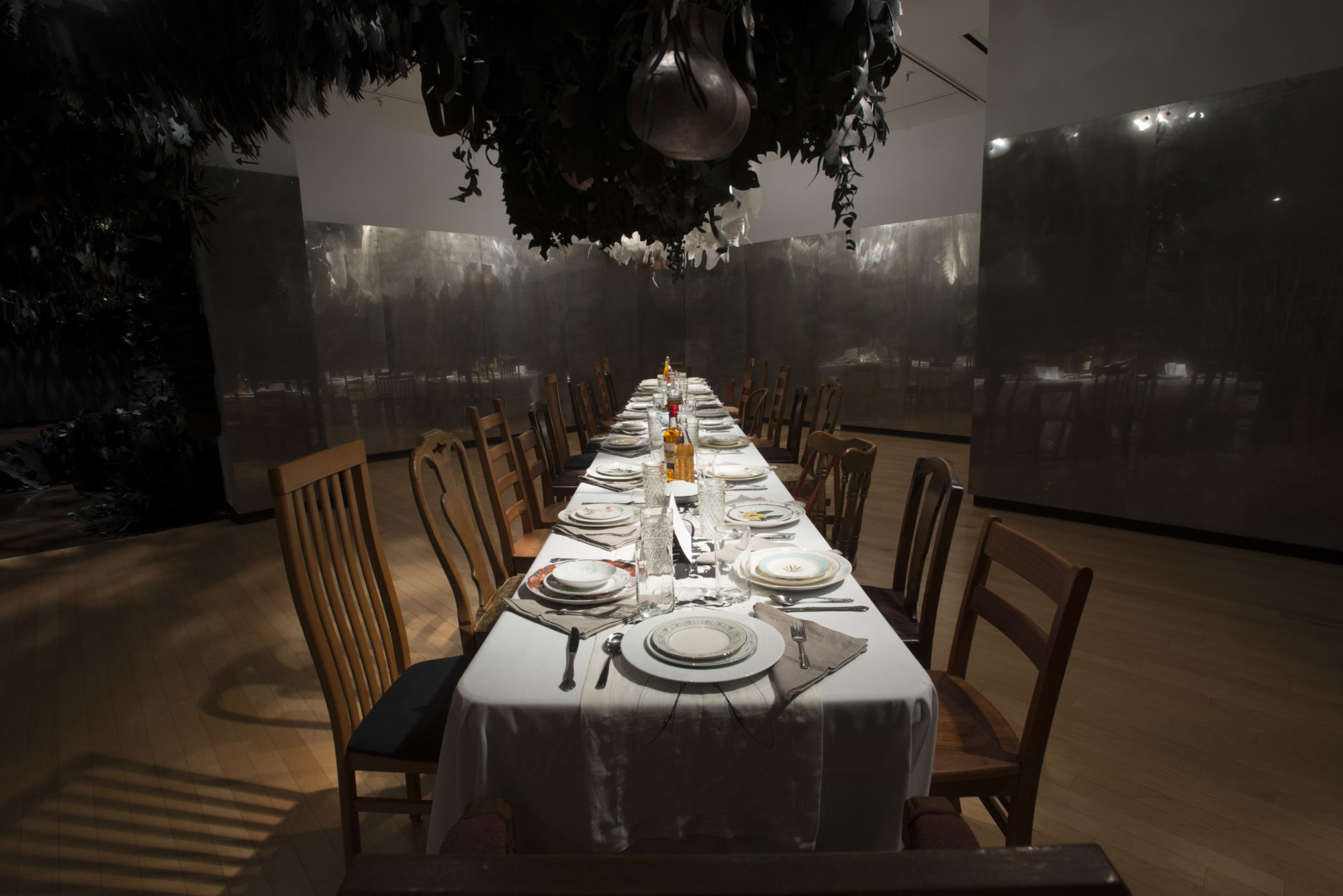 a long dinner table sits beneath dark and light paper plants that are hanging