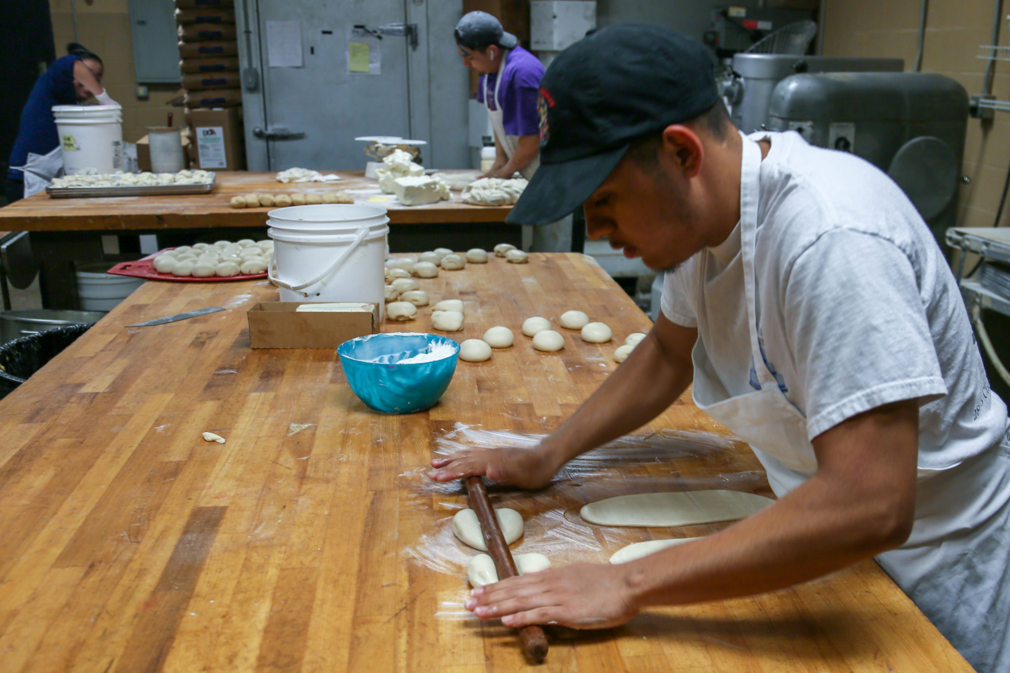 Man rolling dough in the back of a bakery