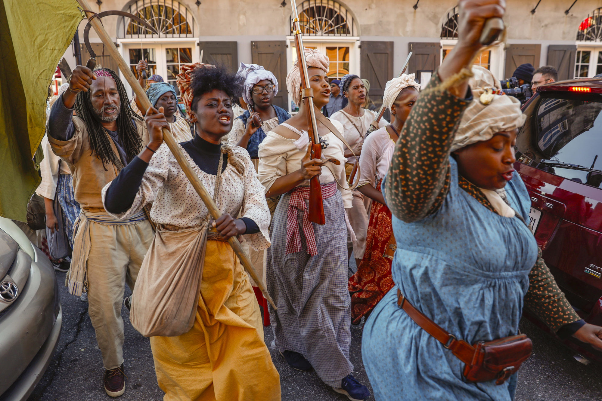 Black men and women in historical dress march through the streets of New Orleans in a slave rebellion reenactment