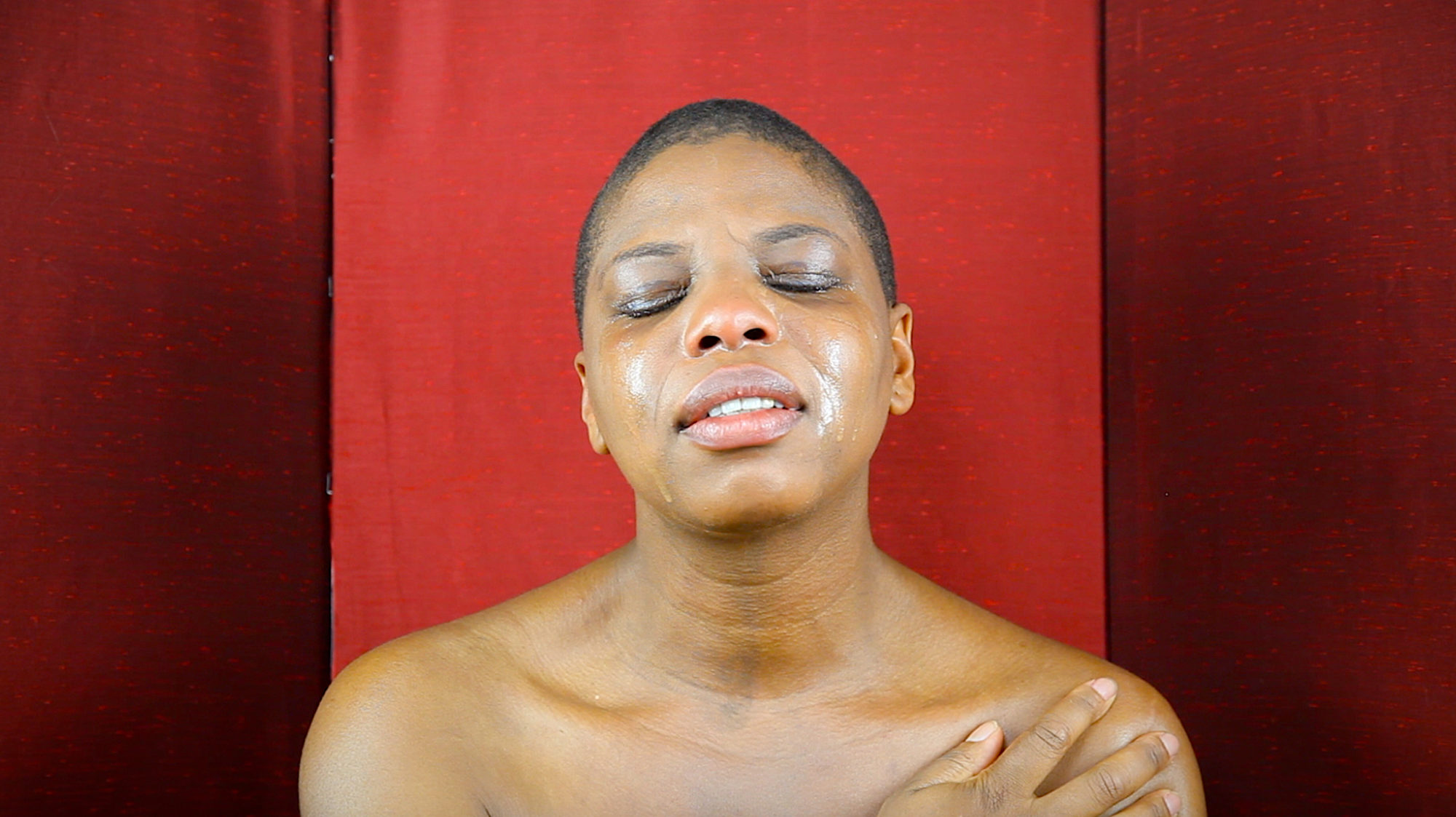 headshot of person in front of red backdrop. person has tears on face and eyes closed