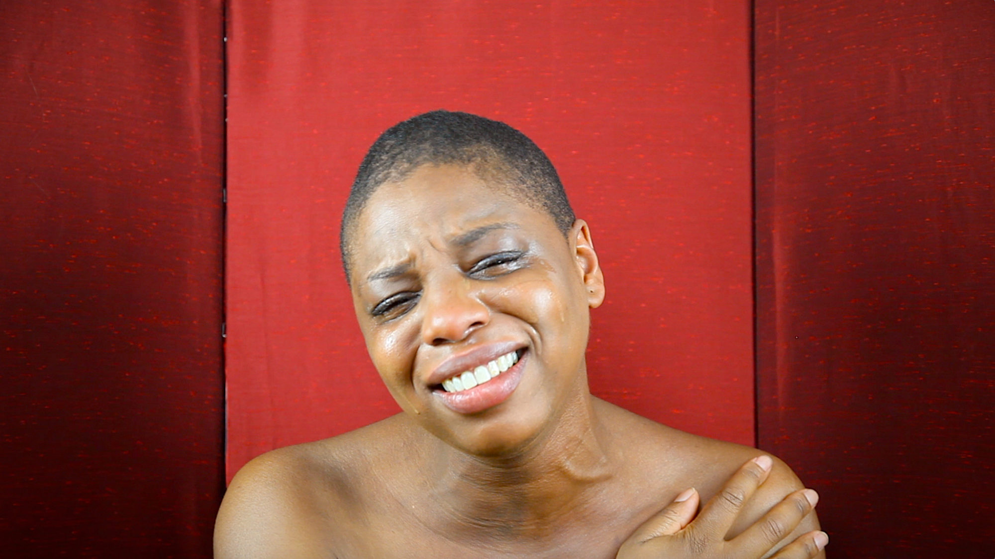 headshot of a person crying while smiling in front of red background