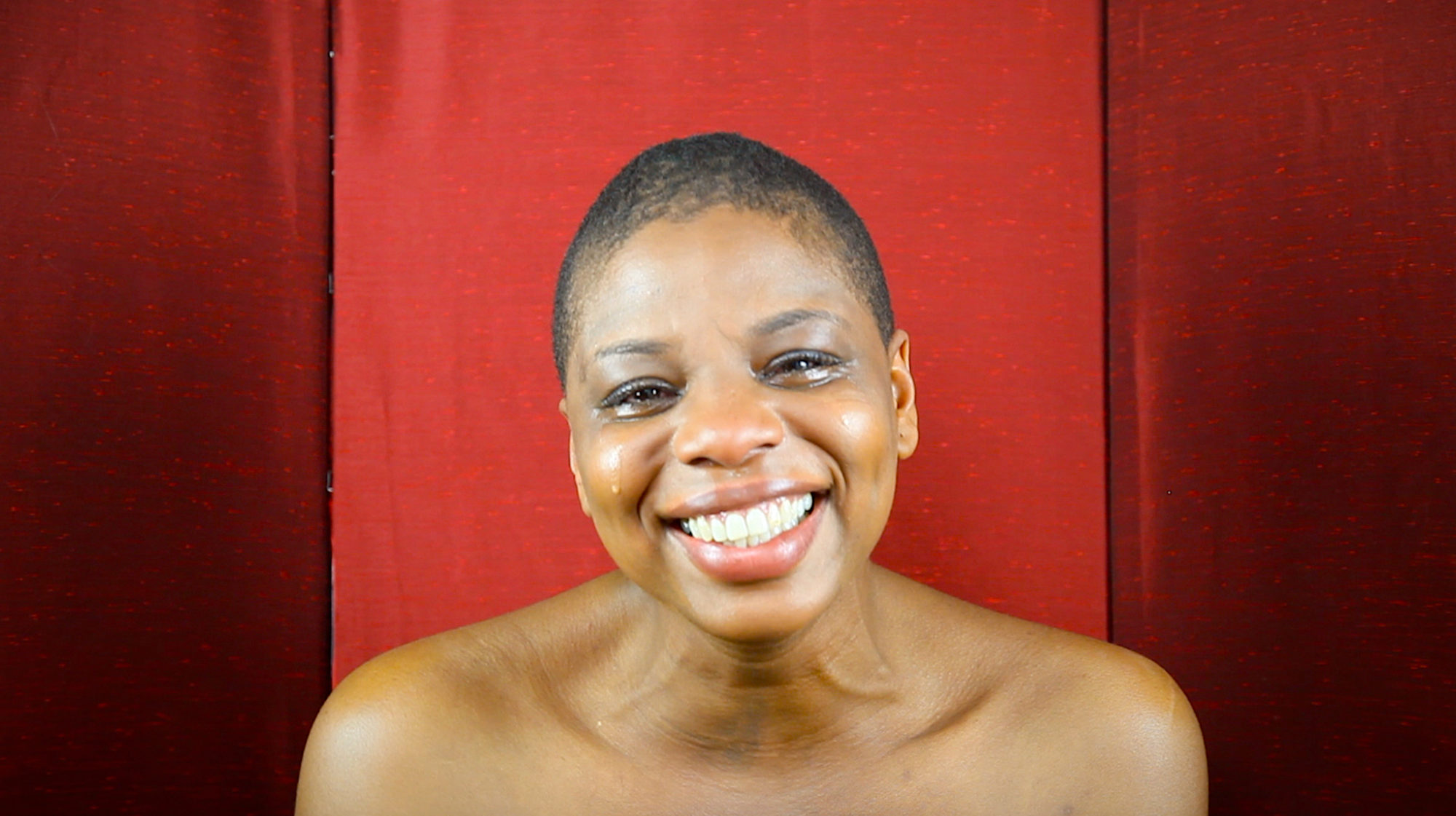 headshot of person crying and smiling in front of red backdrop