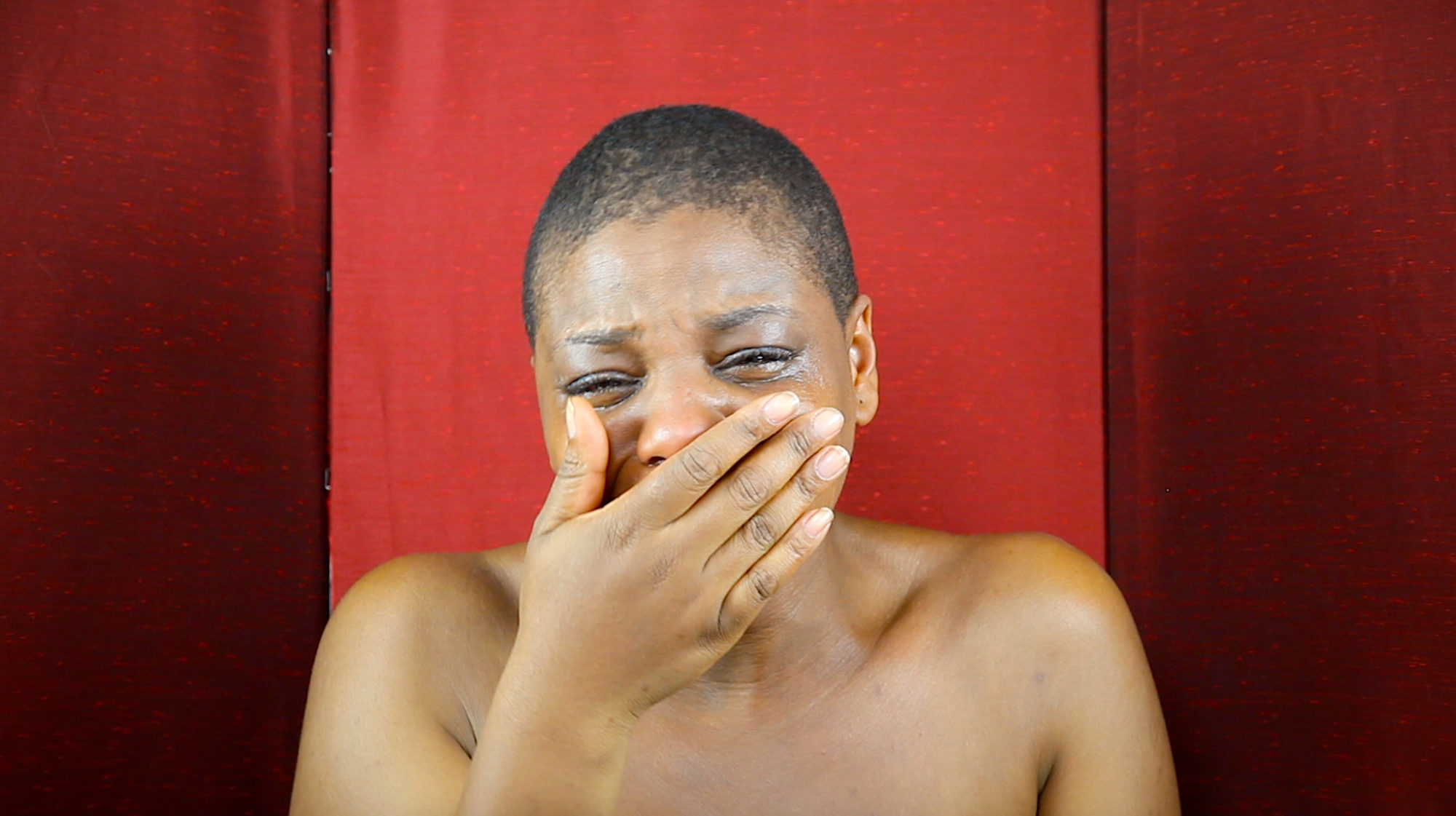 person in front of red backdrop cries and covers mouth with hand