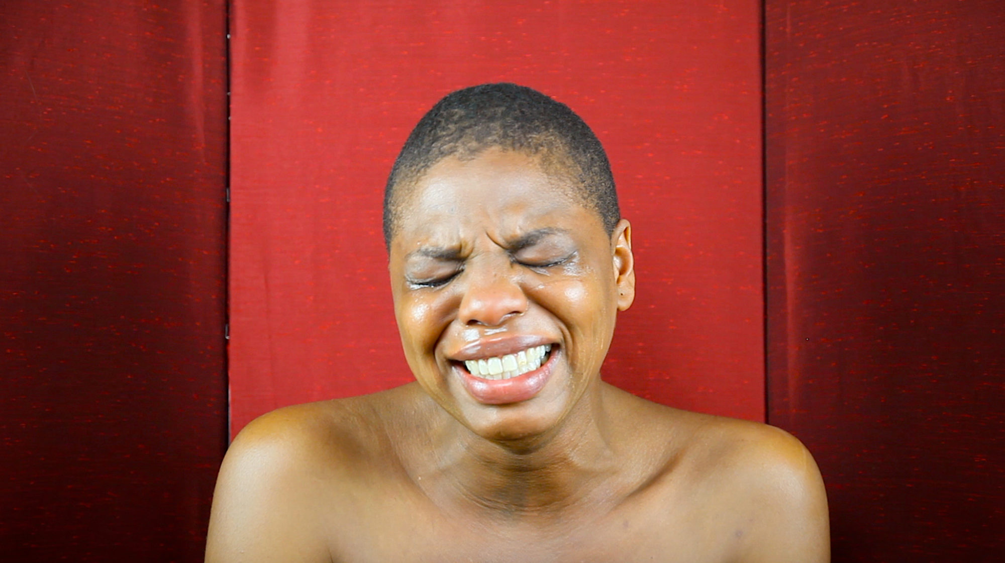 headshot of person crying in front of red backdrop