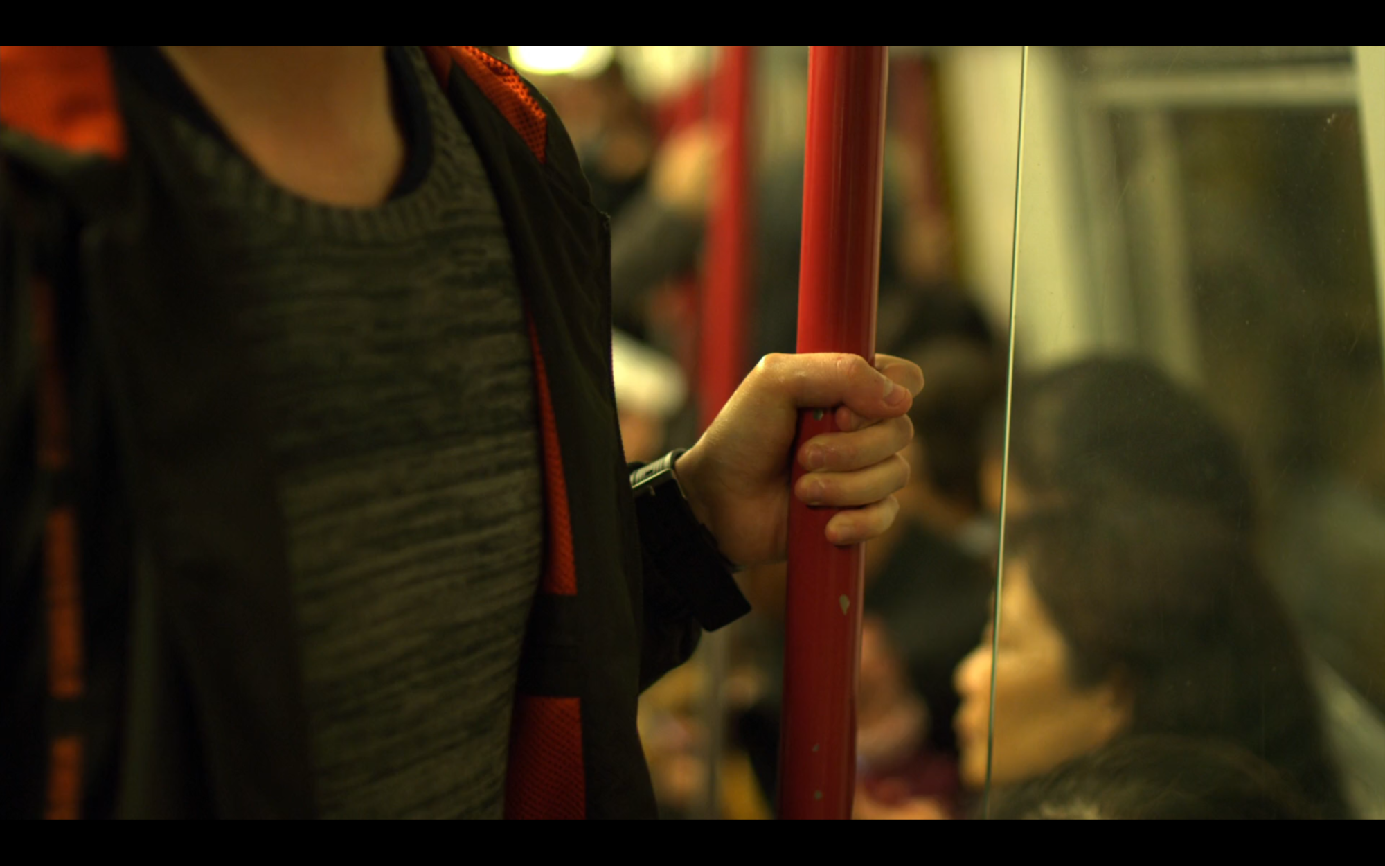 shot of hand in focus holding on to a red pole inside a crowded train car