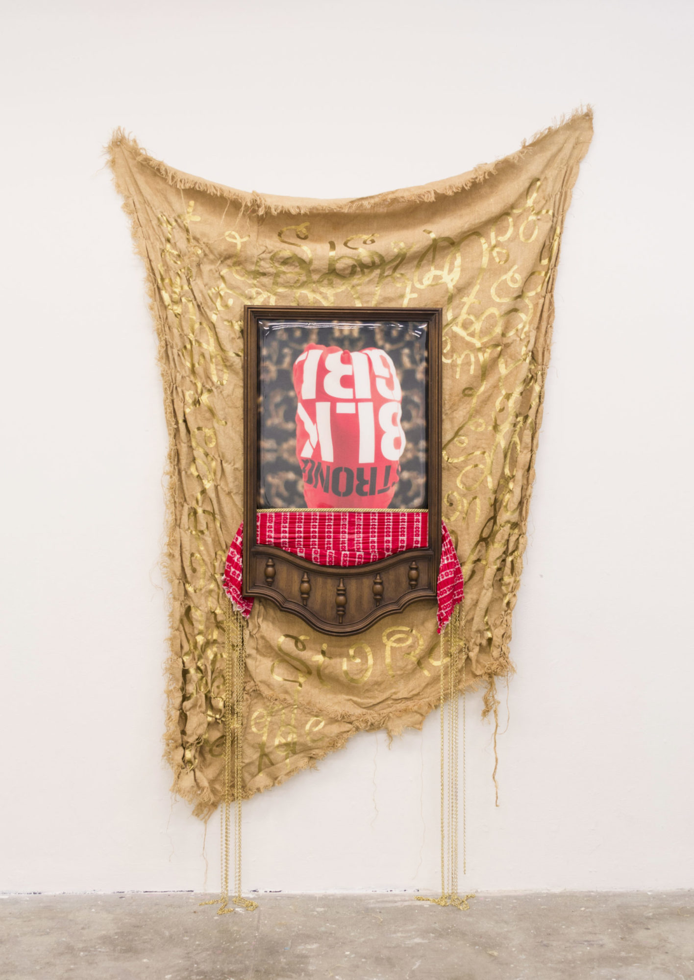 An asymmetrical gold-painted fabric hangs behind a wooden dresser mirror frame; inside the frame is a red checkered tablecloth and a photo