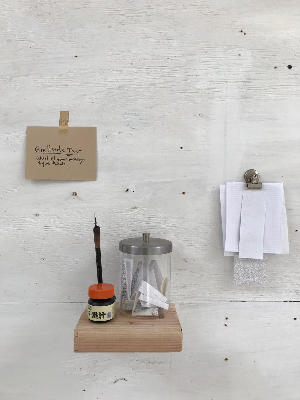 a jar holding messages of gratitude is placed next to paper and ink