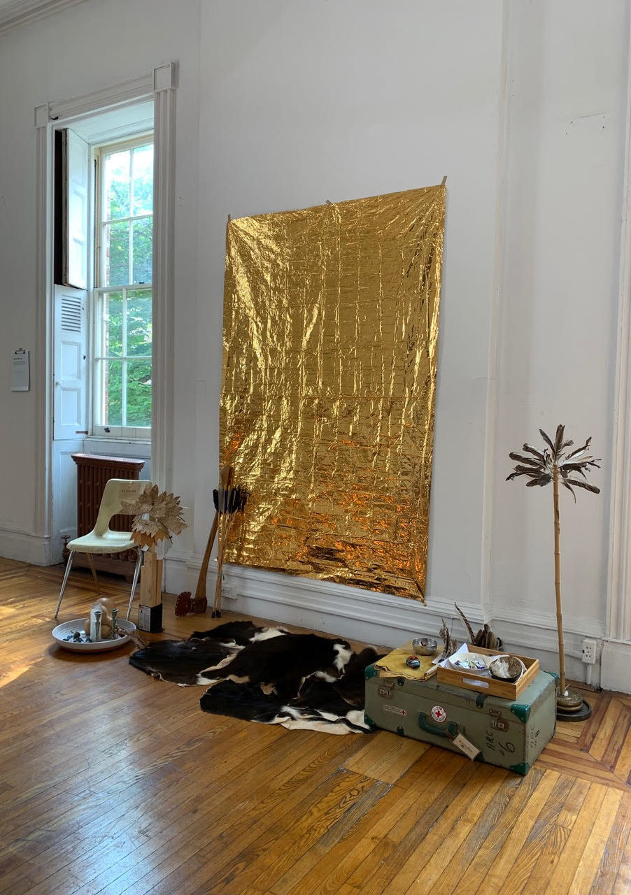 large piece of gold foil hangs on wall. items are placed on the floor beneath it