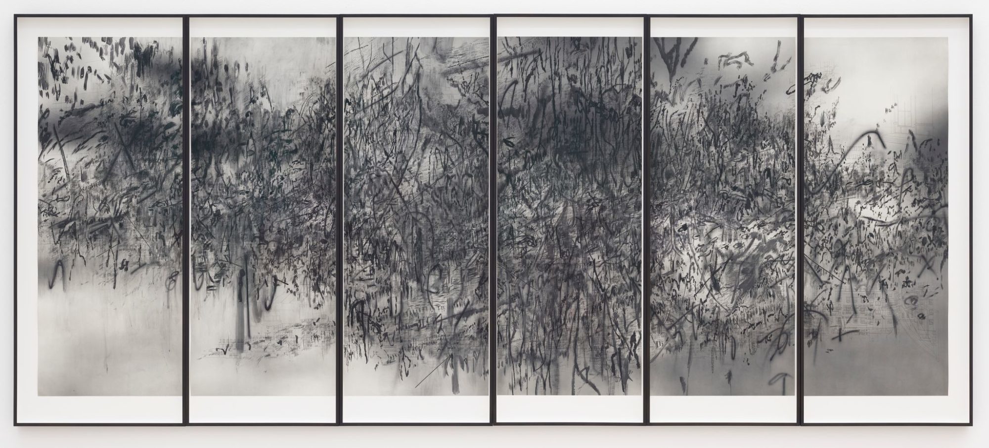 A photograph of a black and white work consisting of six vertical panels. The panels have smudged lines and a denser texture closer to the center of the panels.
