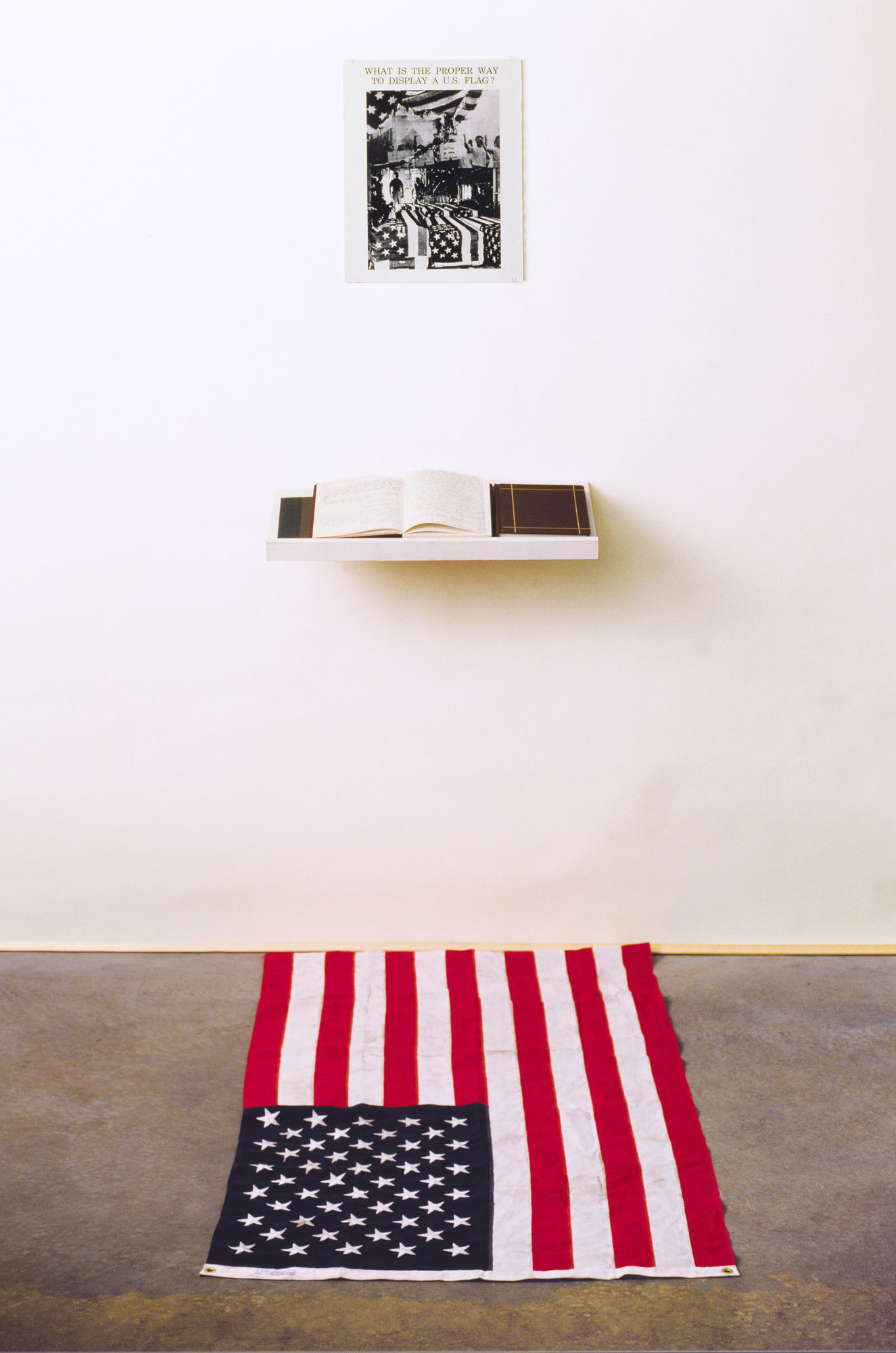 American flag on floor below open book and poster on wall.