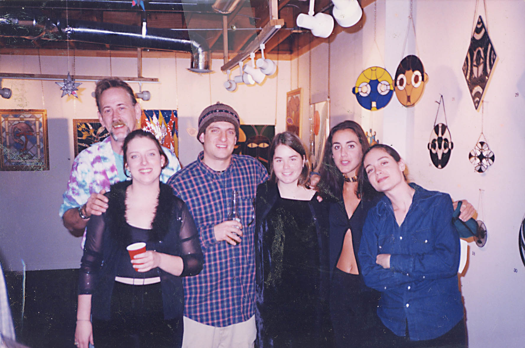 A photograph of six individuals standing together in Young Blood Gallery. Several pieces of hanging and mounted artwork are in the background.